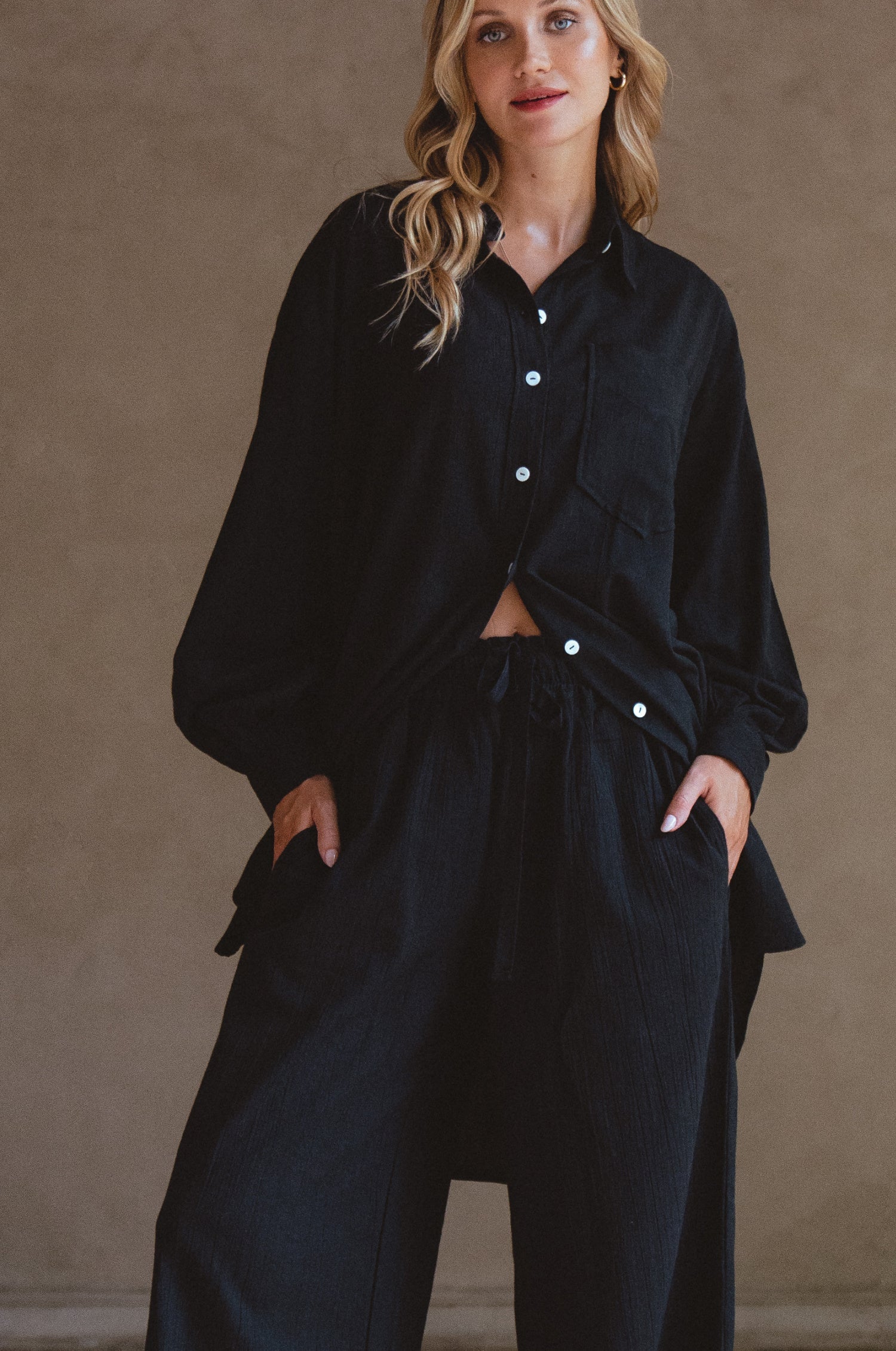 Woman wearing a black outfit with white buttons against a beige background