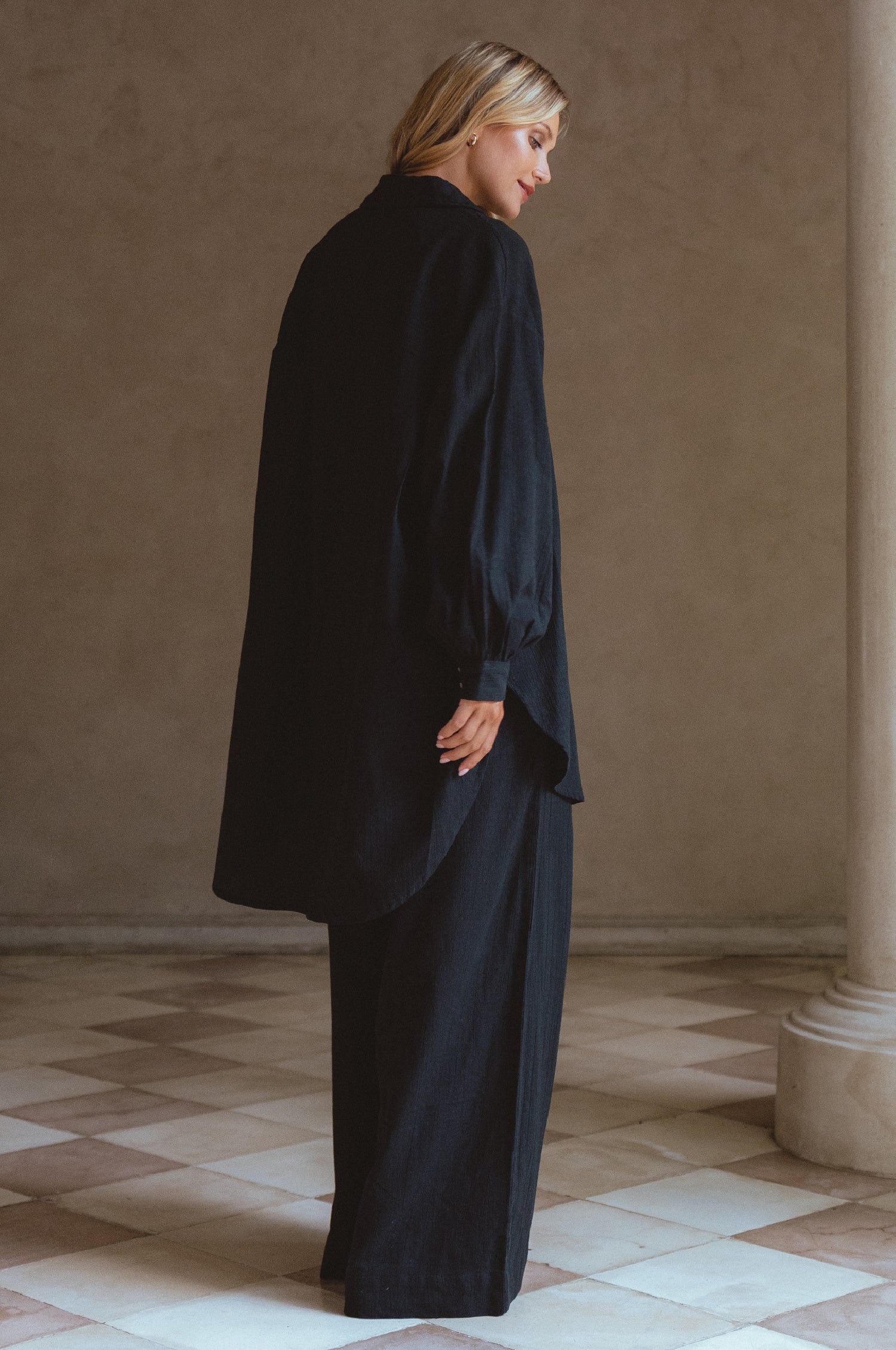 Woman wearing a black outfit standing in a room with beige walls and tiled floor.