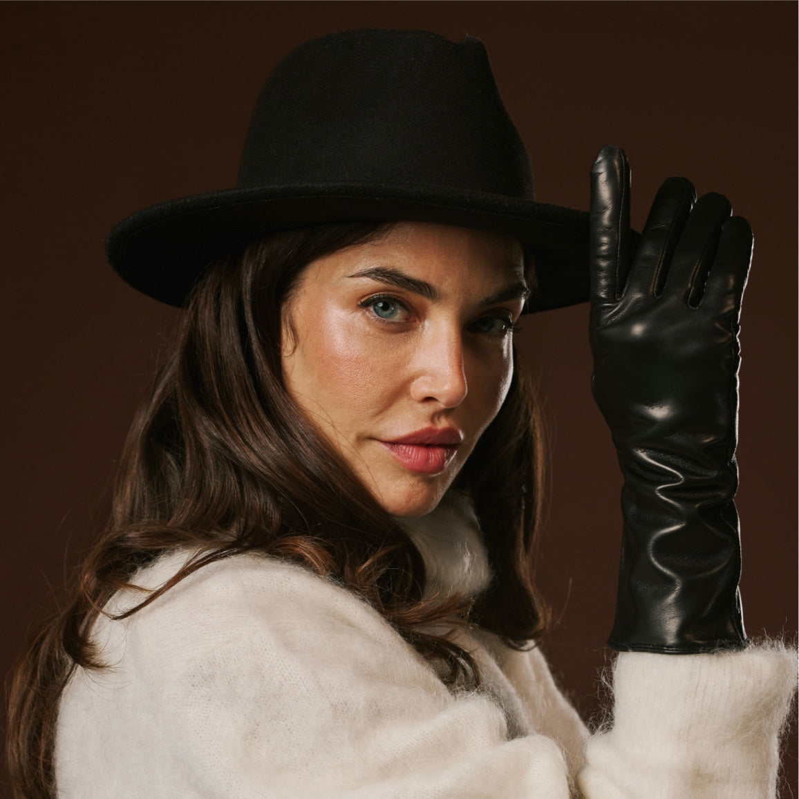 Woman wearing a black hat and leather glove against a brown background