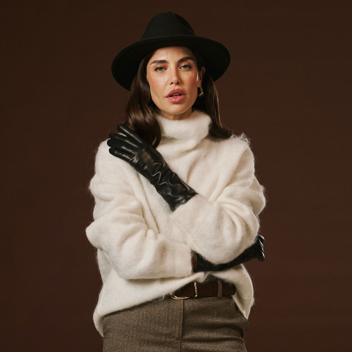 Woman wearing a white fur coat, black hat, and gloves against a brown background