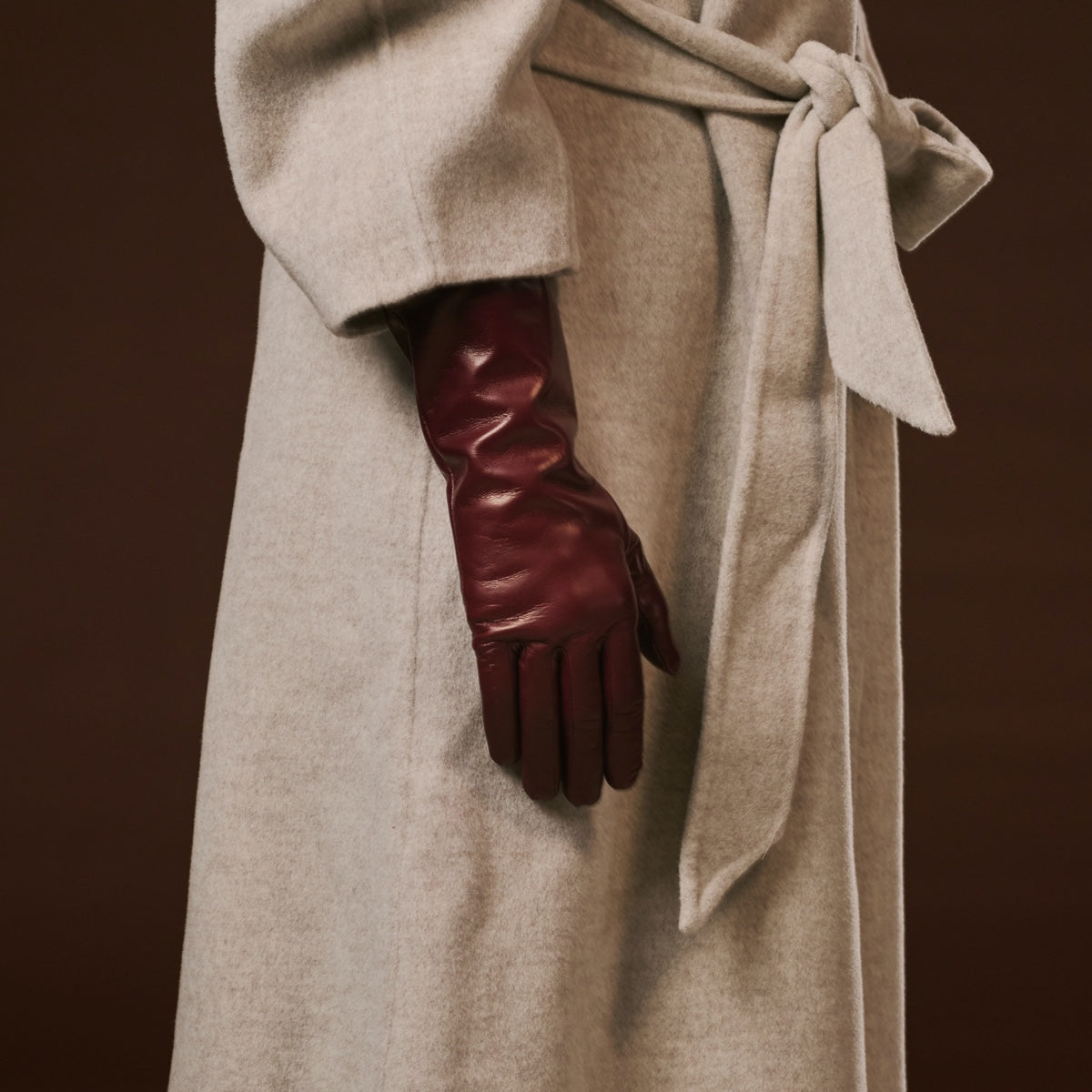 Beige coat with a hand wearing a burgundy leather glove on a brown background