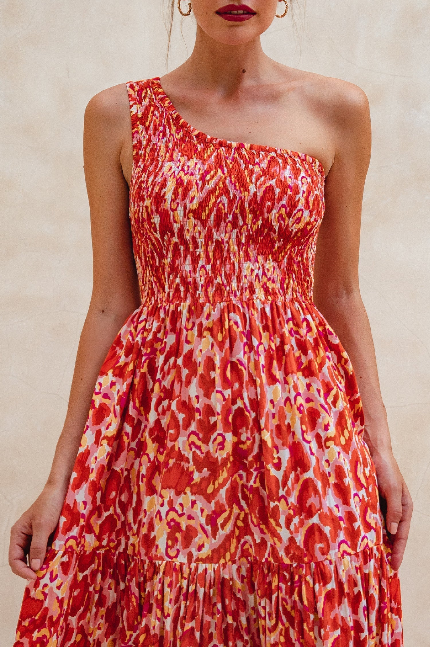 Woman wearing a red and orange patterned one-shoulder maxi dress against a neutral background, front view closeup