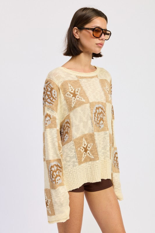 Woman wearing a cream and taupe patchwork knit sweater with star and seashell motifs, front view. and brown knee-high boots on a white background
