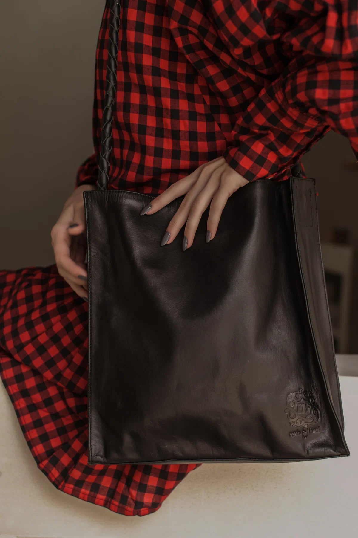Person wearing a red and black checkered outfit holding a black leather bag.