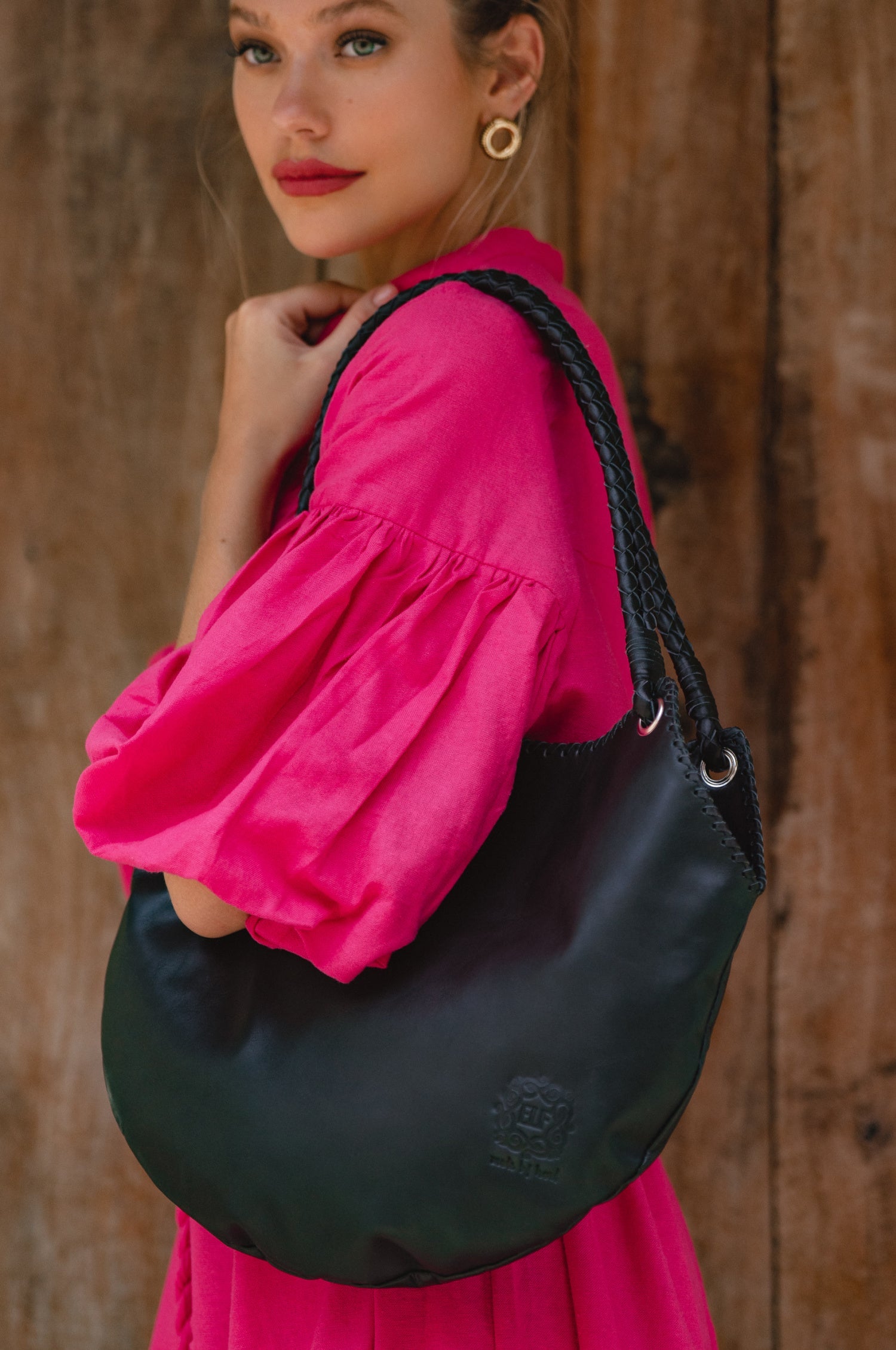 Woman in a pink outfit holding a black leather tote bag against a wooden background