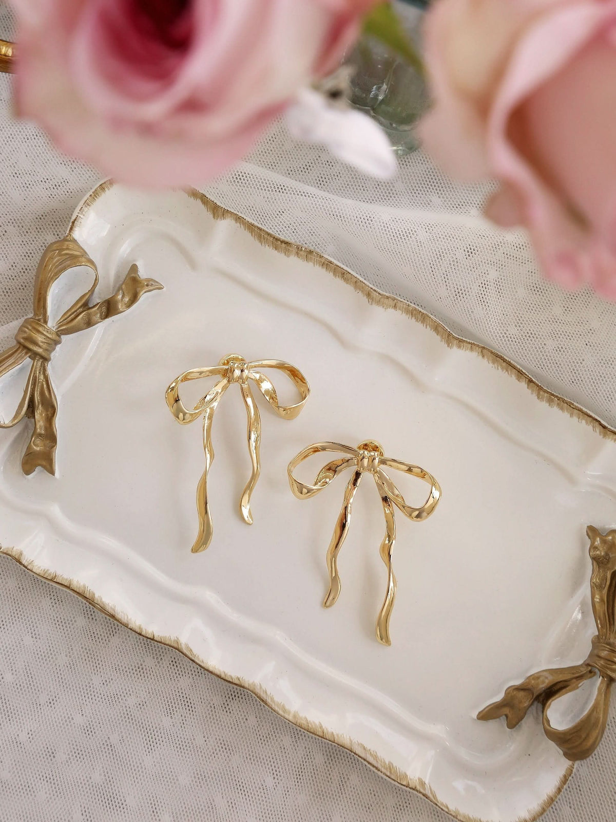 Gold-tone bow earrings flat lay with roses, lace and coordinating bow necklace.
