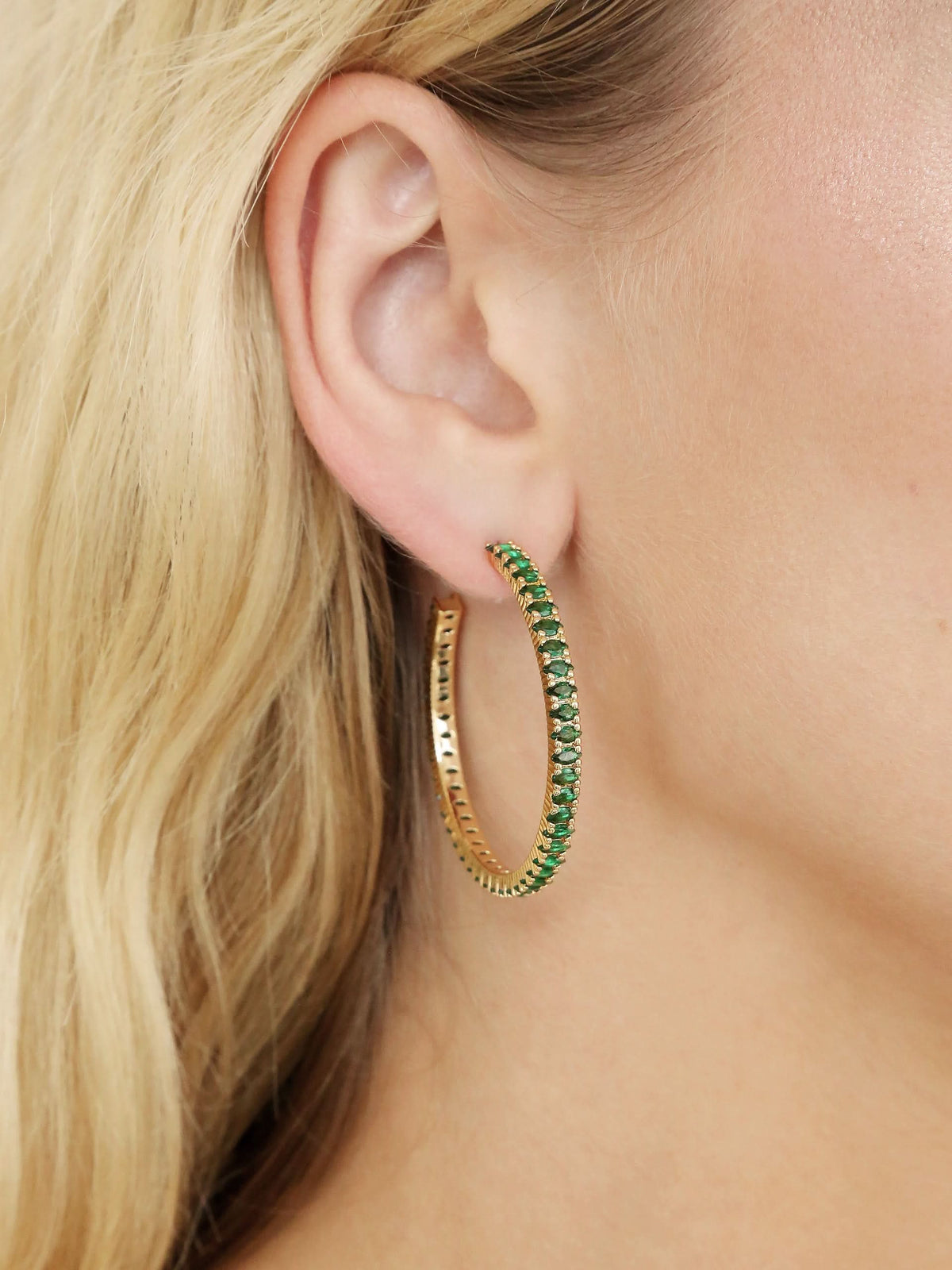 Close-up of woman wearing green stone hoop earring with gold-tone setting.