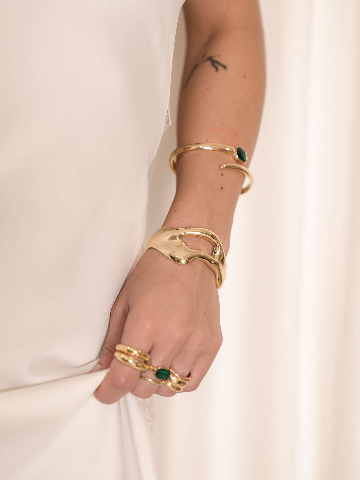 Woman wearing gold-tone crystal wrap ring and green-accented bracelets.