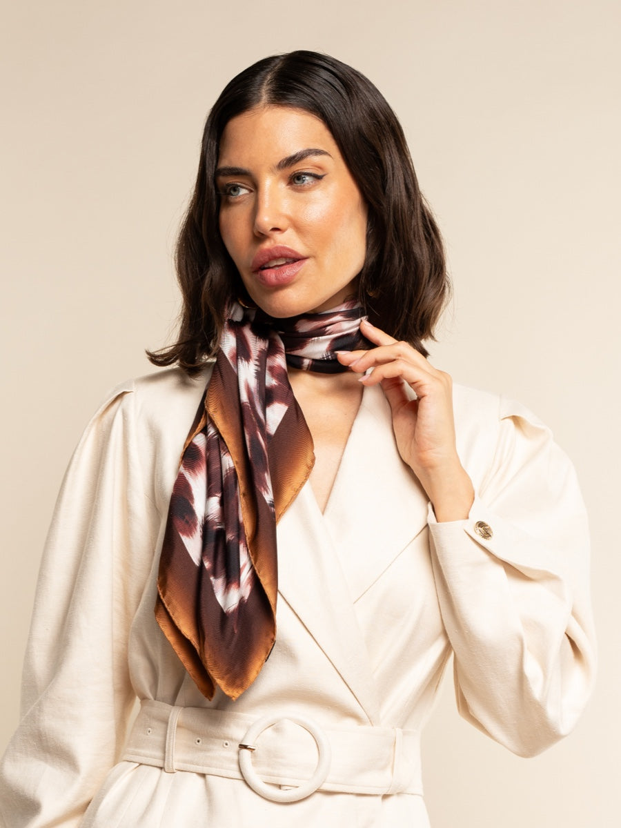 Woman wearing a patterned silk scarf around her neck against a beige background