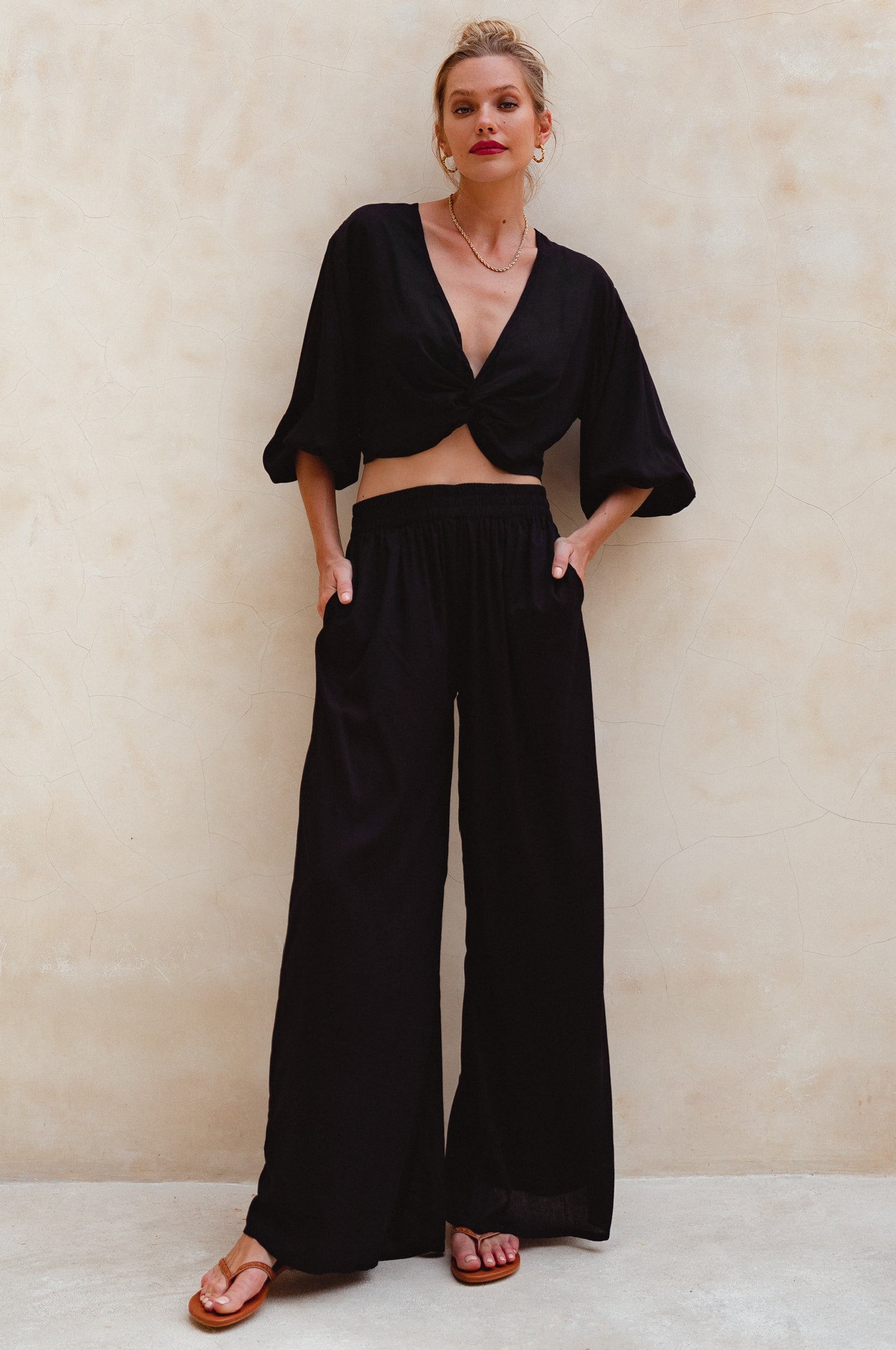 Woman wearing a black outfit with wide-leg pants against a beige background