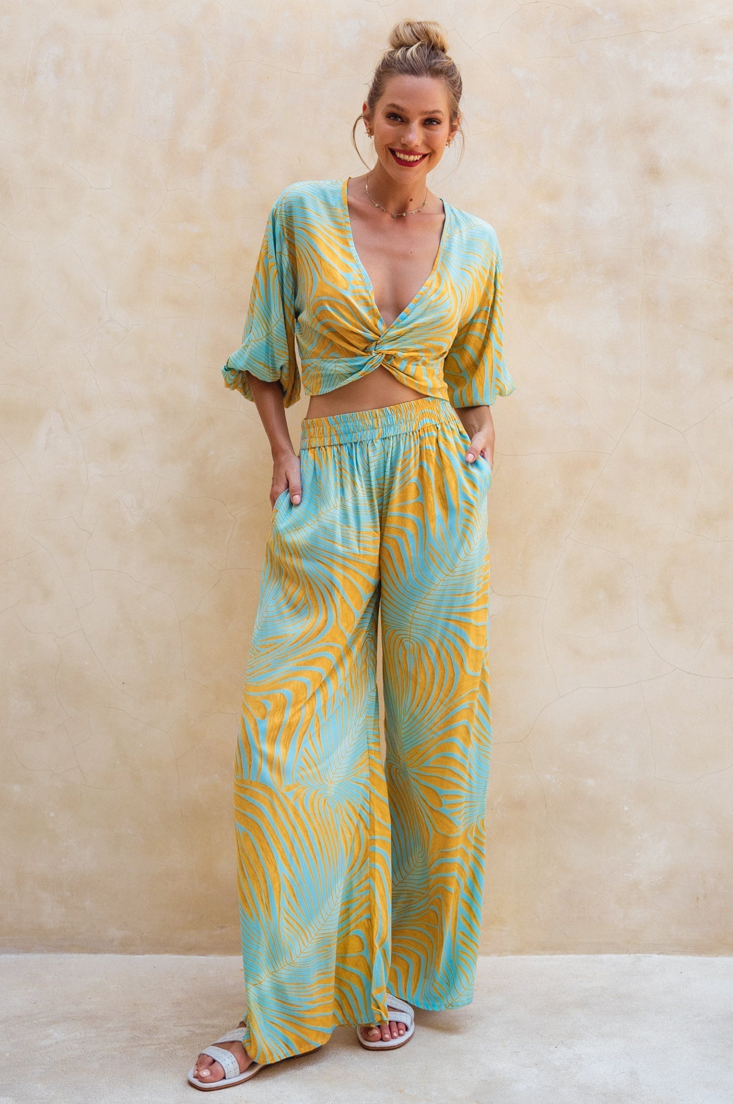 Woman wearing a yellow and blue patterned outfit against a beige wall.
