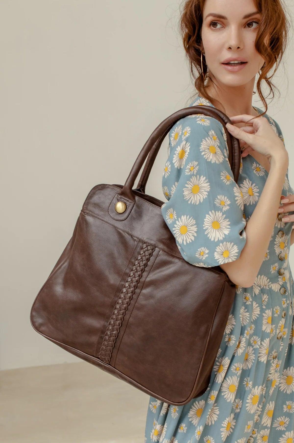 Woman holding a brown leather handbag against a neutral background