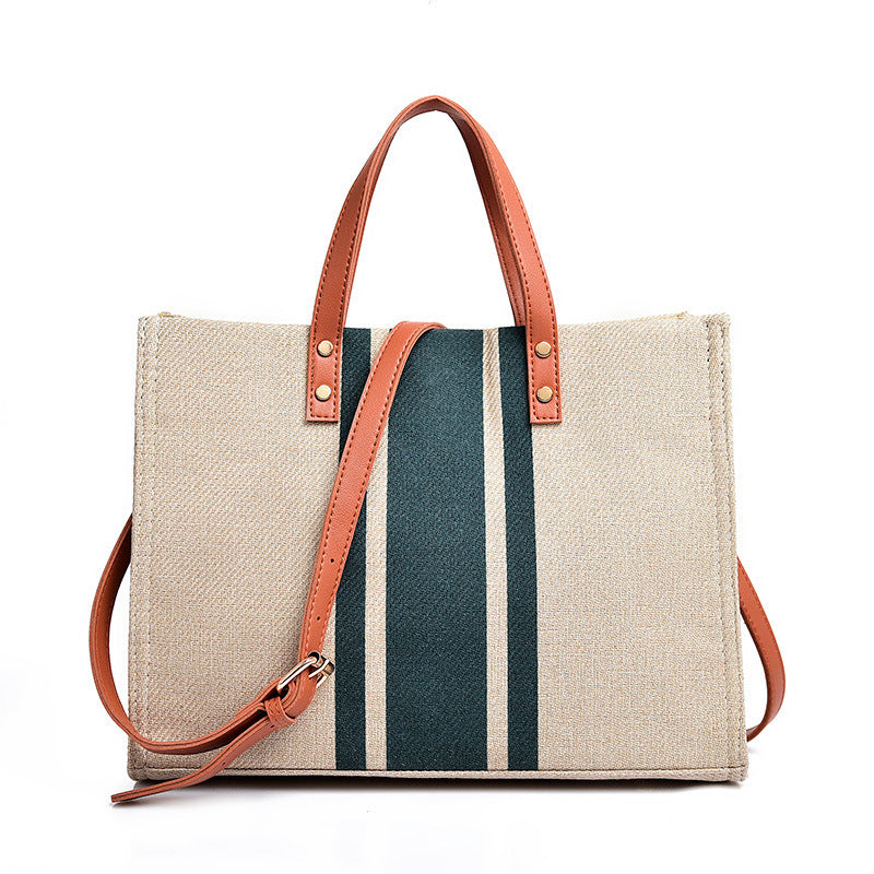 Beige tote bag with brown handles and strap, featuring blue and white stripes on a white background.