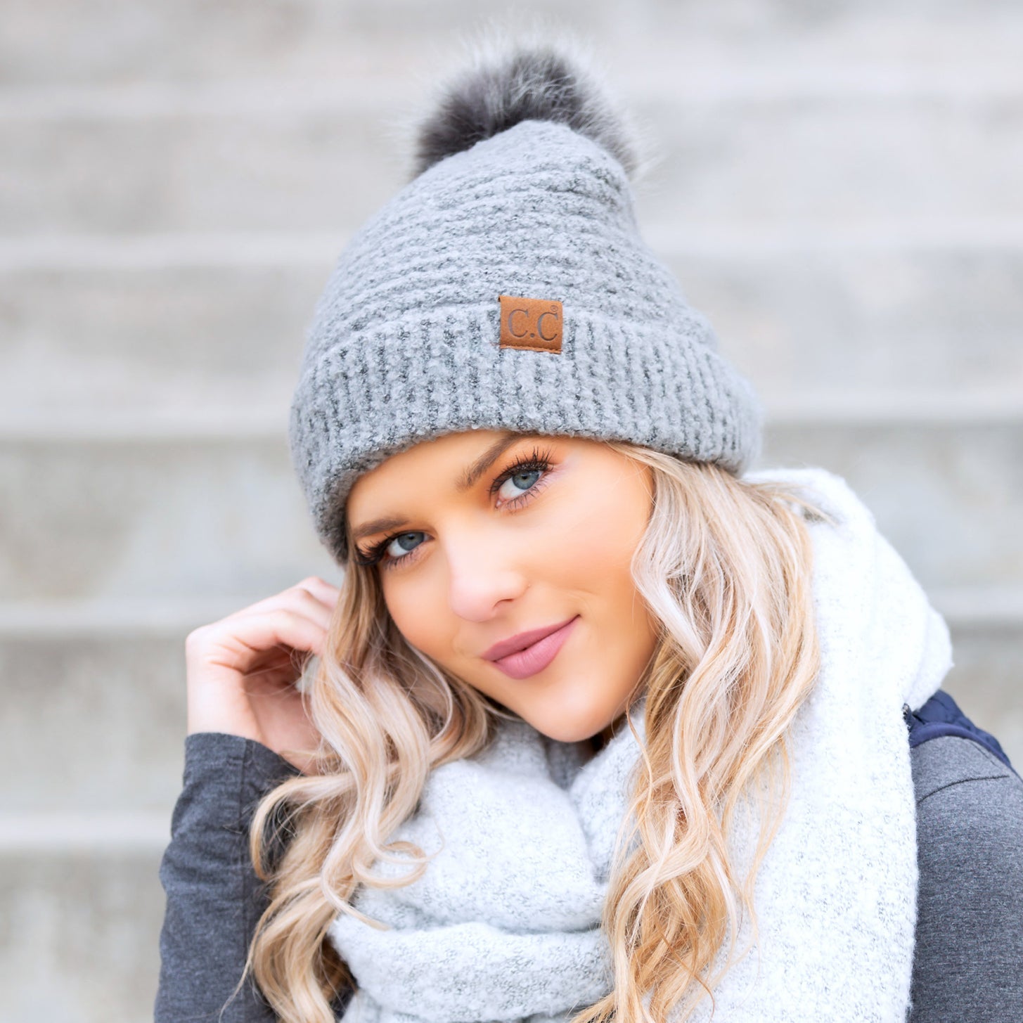 gray boucle knit hat with faux fur pom worn with scarf, angled view