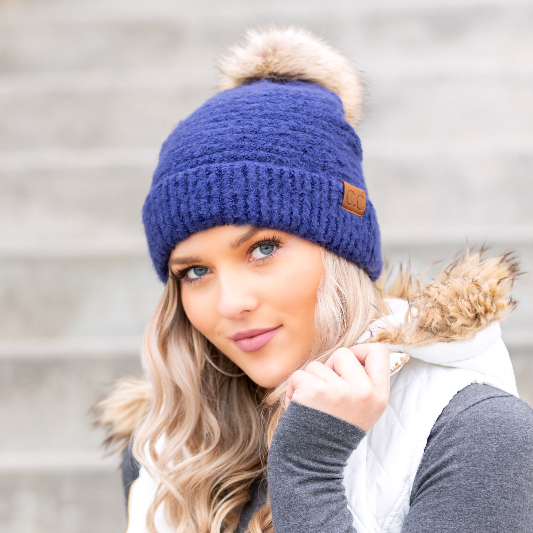 Evening Blue boucle knit hat with faux fur pom worn with scarf, angled view
