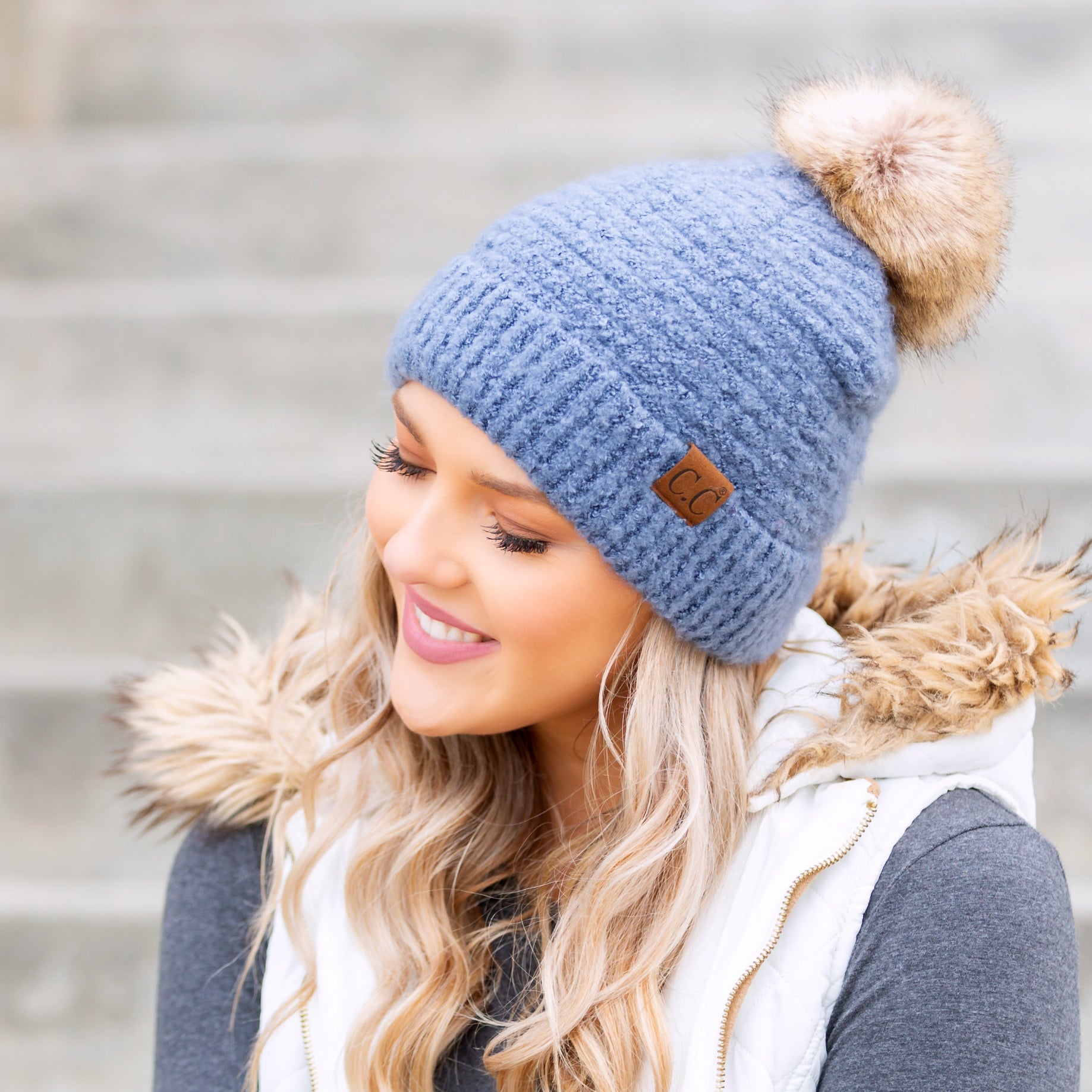 light blue boucle knit hat with faux fur pom worn with scarf, angled view