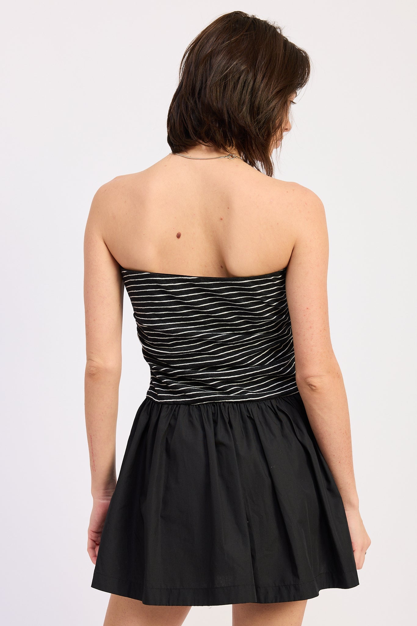 Woman wearing a black strapless mini dress striped bodice contrast skirt on a white background