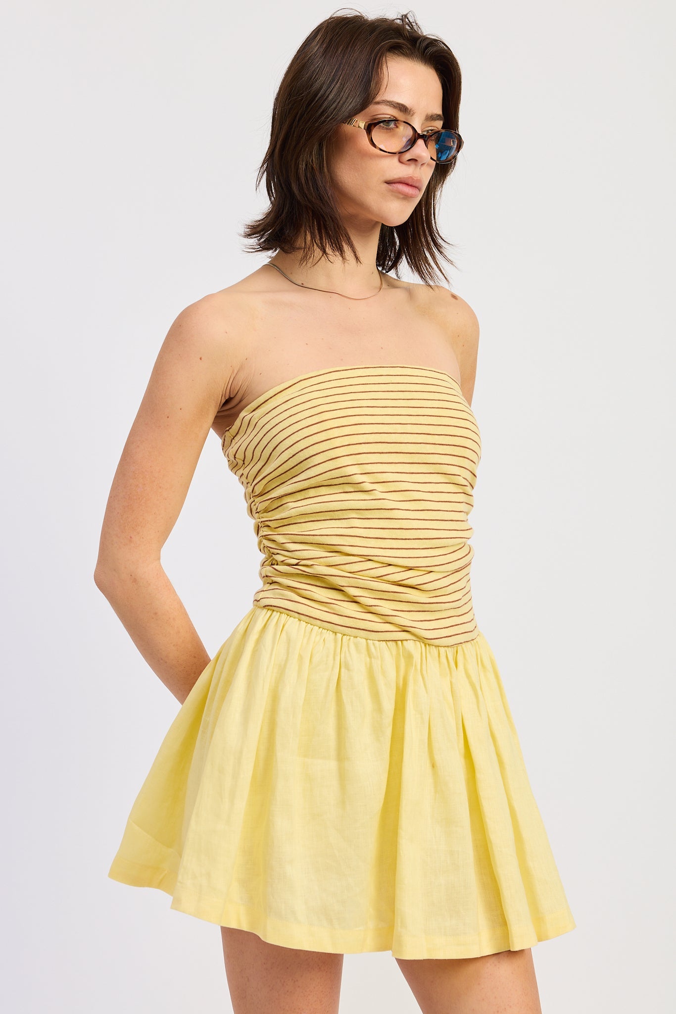 Woman wearing a yellow strapless mini dress striped bodice contrast skirt on a white background