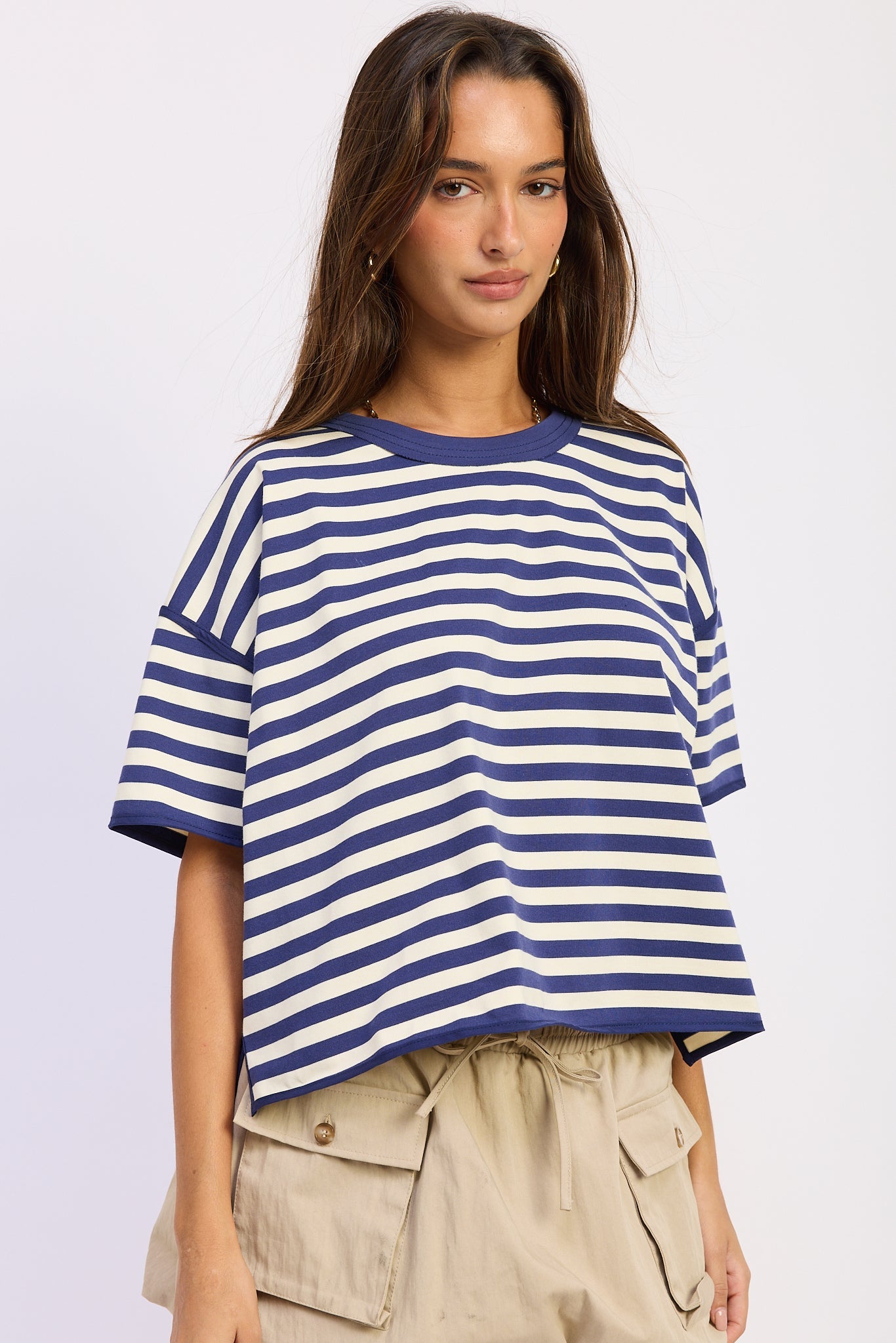 Woman wearing a blue and white striped shirt with light blue jeans on a plain background