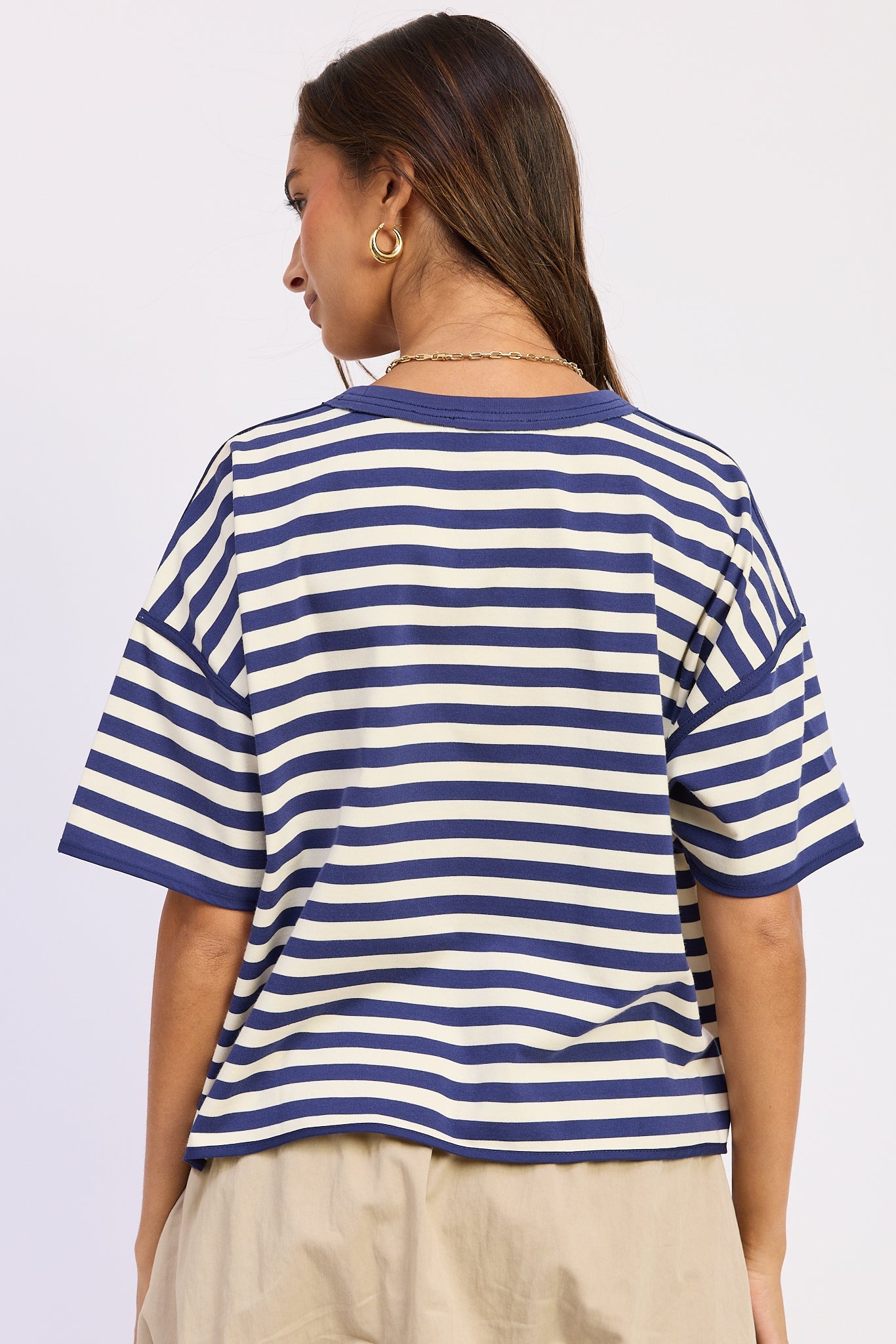 Woman wearing a blue and white striped shirt with light blue jeans on a plain background back view