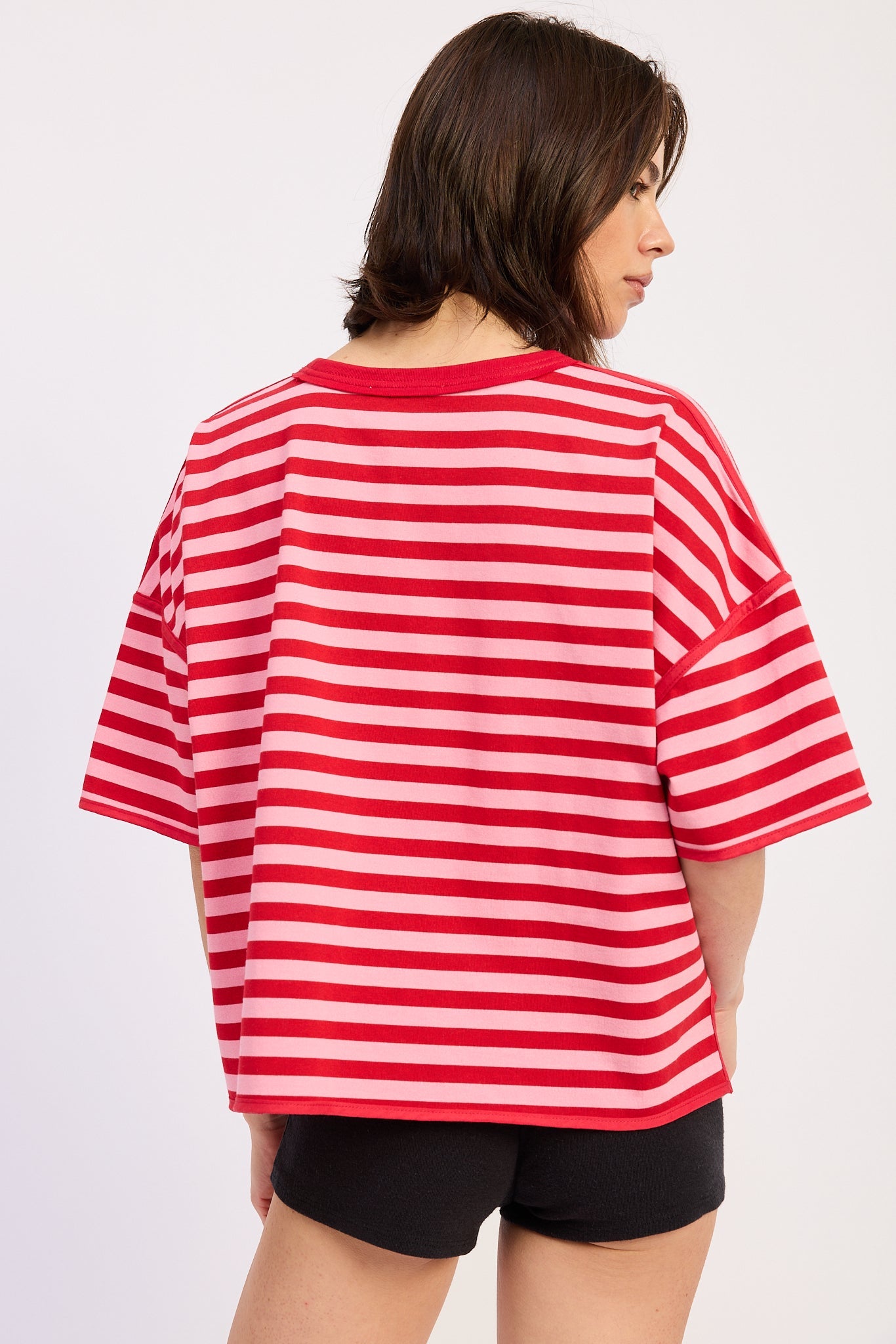 Woman wearing a red and pink striped shirt with light blue jeans on a plain background back view
