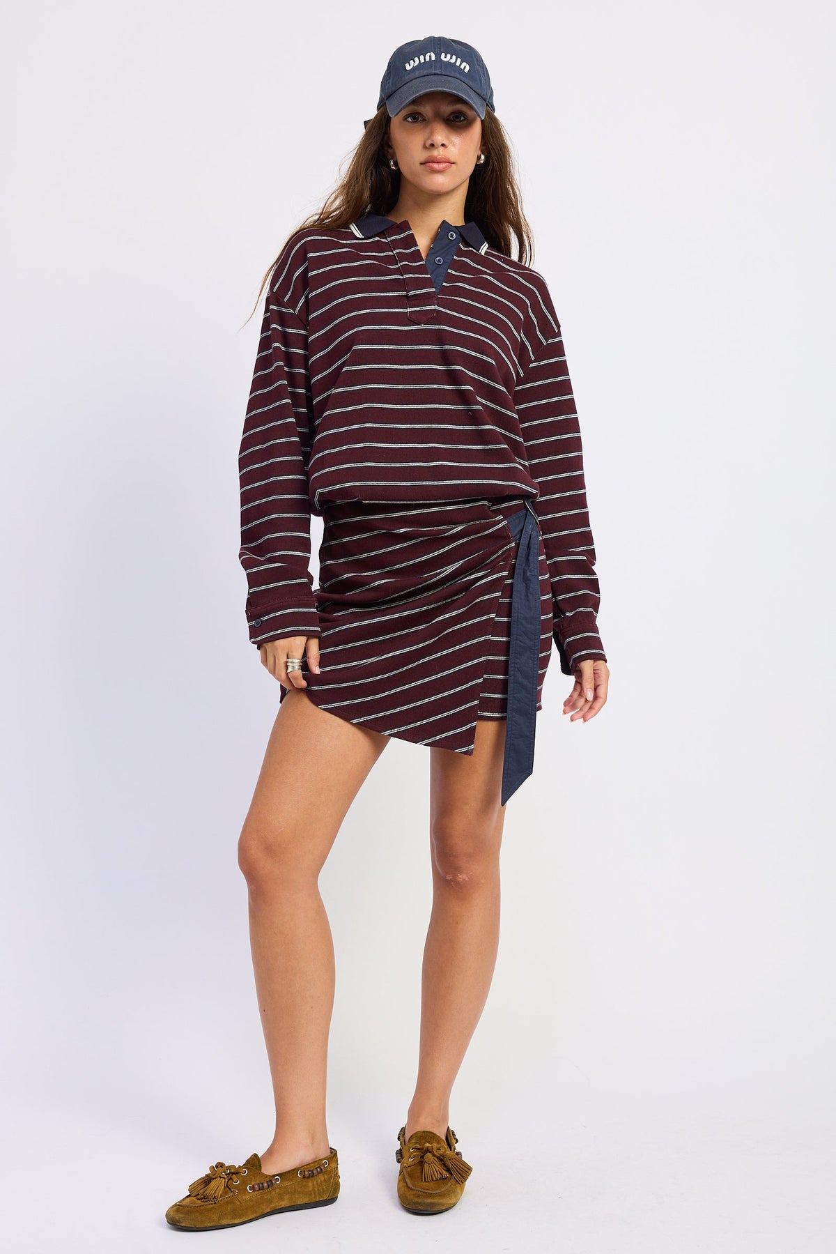 Full-length front view of burgundy striped polo mini dress styled with navy baseball cap and brown loafers.