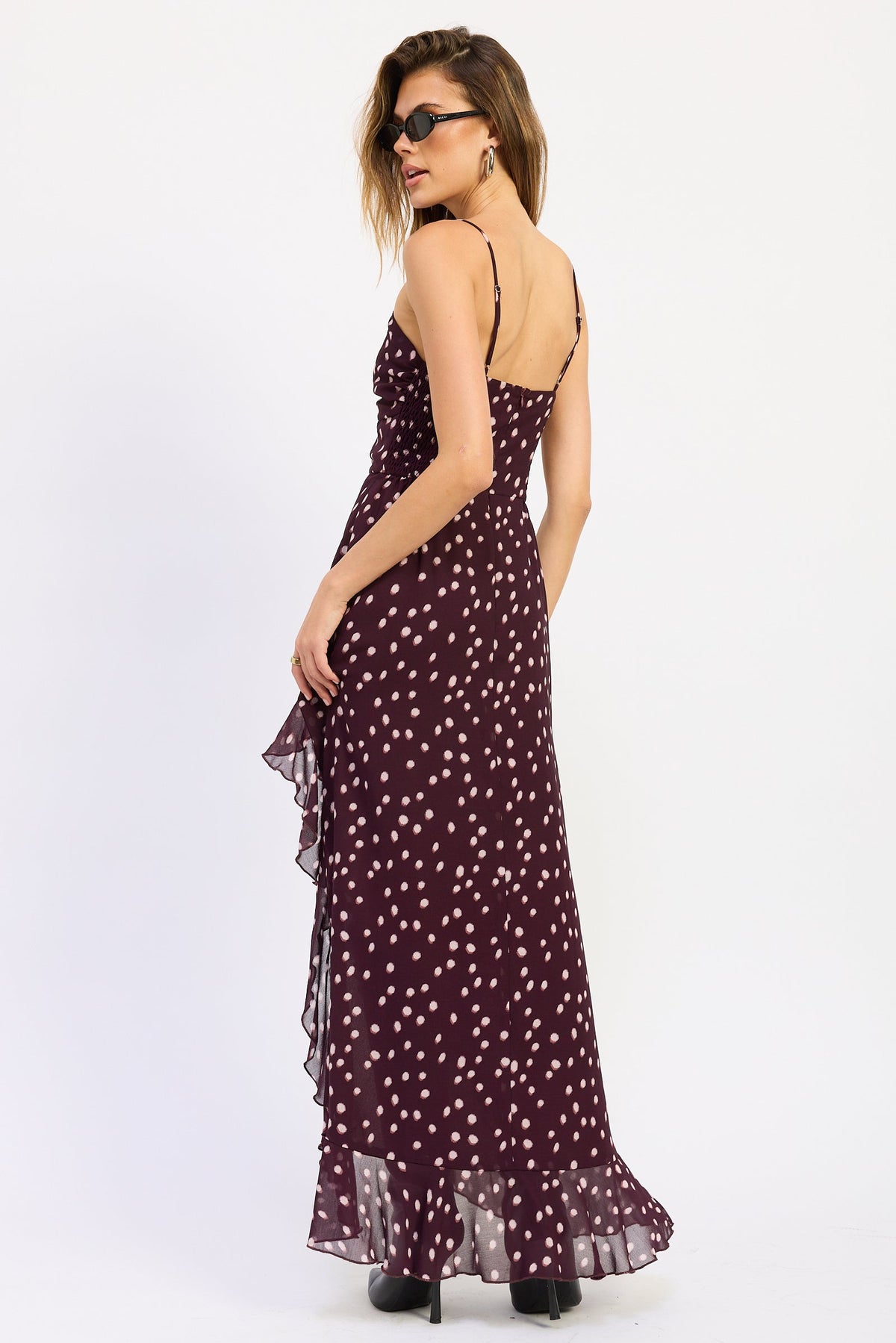 Woman wearing polka dot maxi dress with spaghetti straps and ruffled asymmetric hem in Wine.
