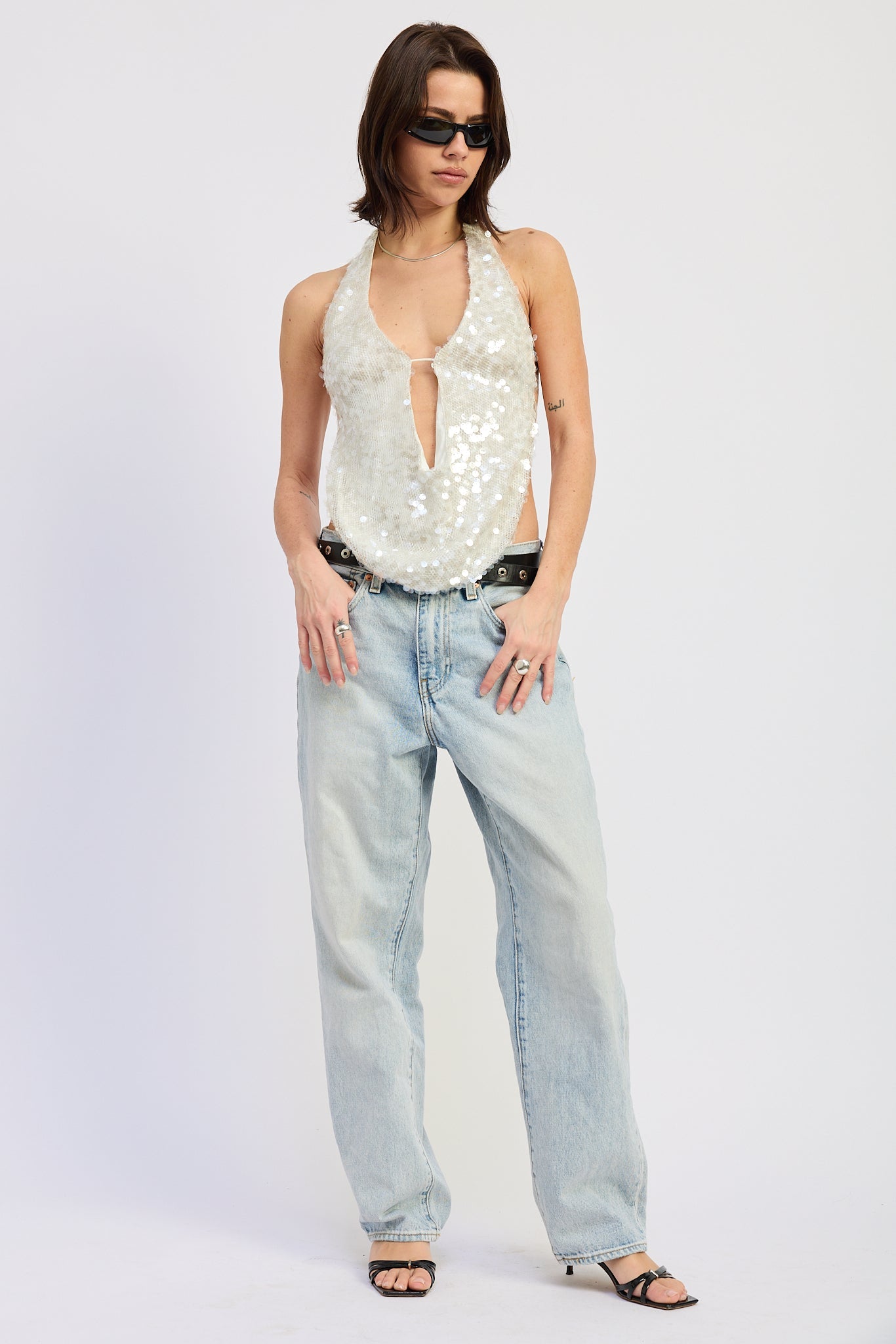 Woman wearing a white sequin halter top and jeans on a plain background front view