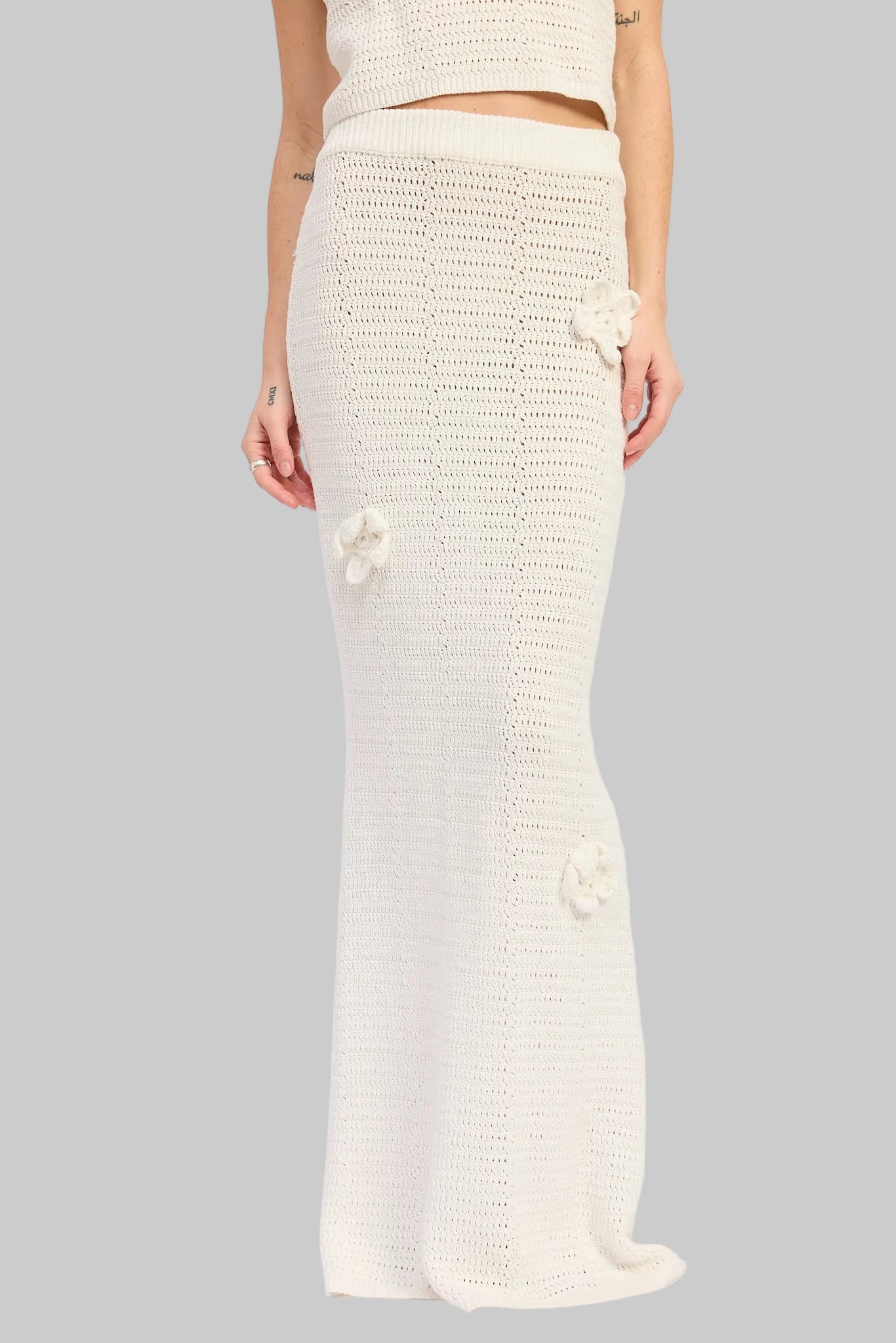 Woman wearing an ivory crochet top and ivory crochet maxi skirt with floral applique details set on a white background