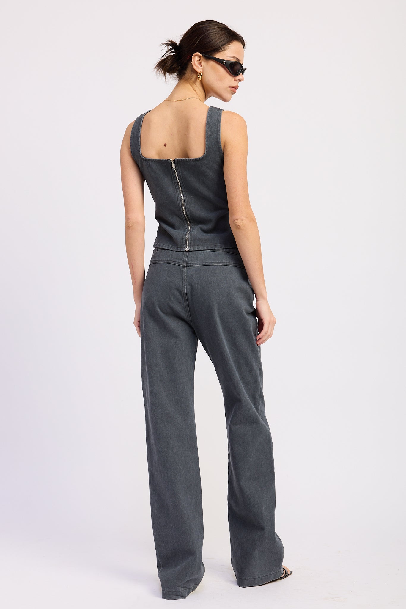 Woman wearing a washed charcoal denim corset top with buckle detail back view with sunglasses on a plain background