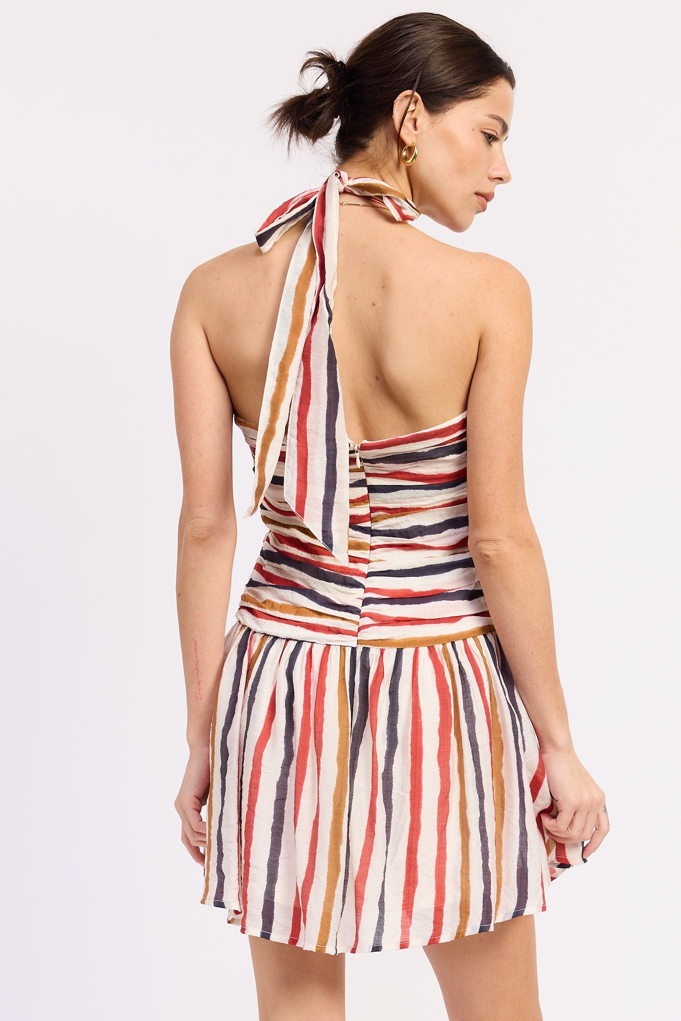 Woman wearing a striped halter mini dress front view with multicolor vertical stripes on a white background back view