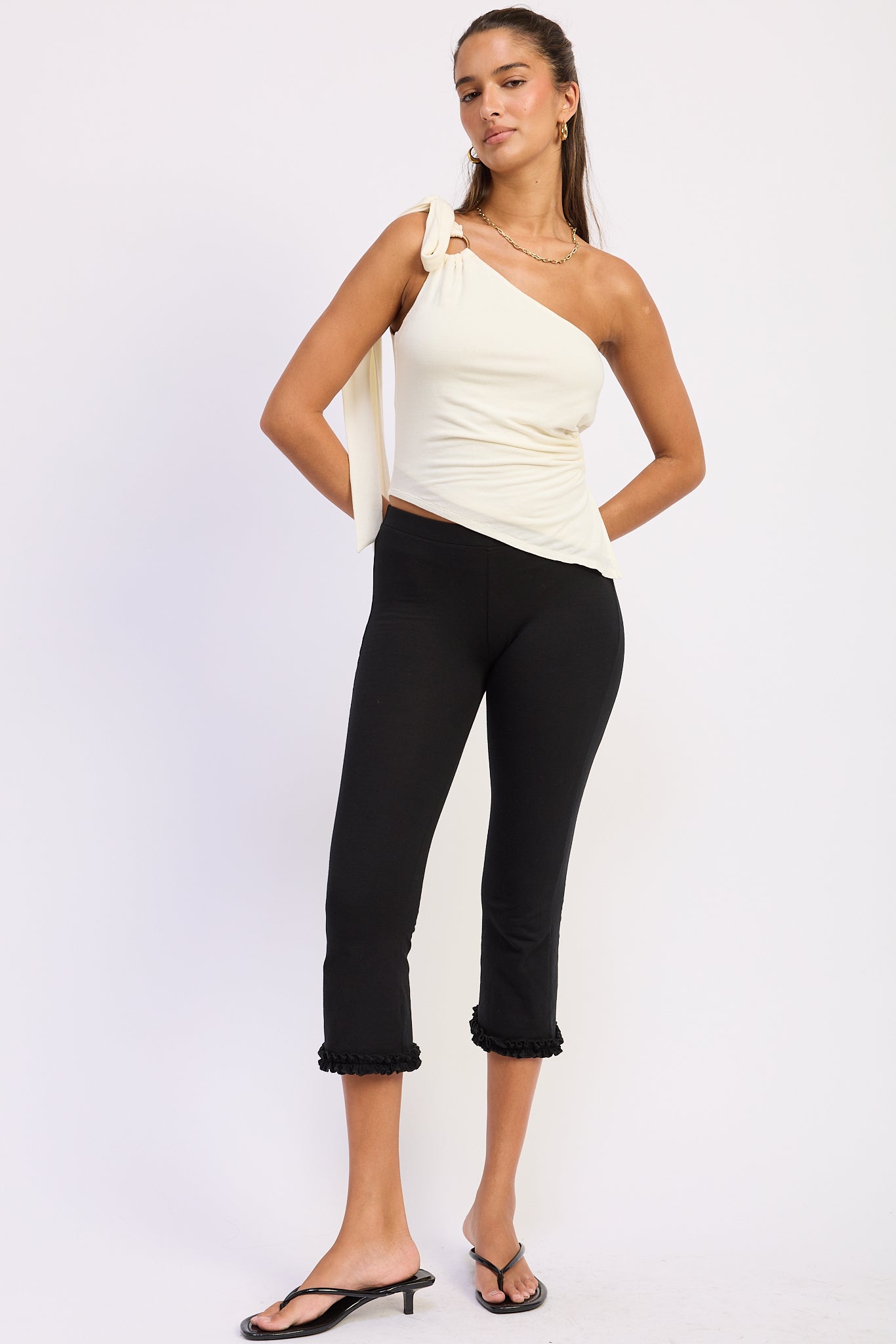 Woman wearing a white one-shoulder top and black pants on a white background