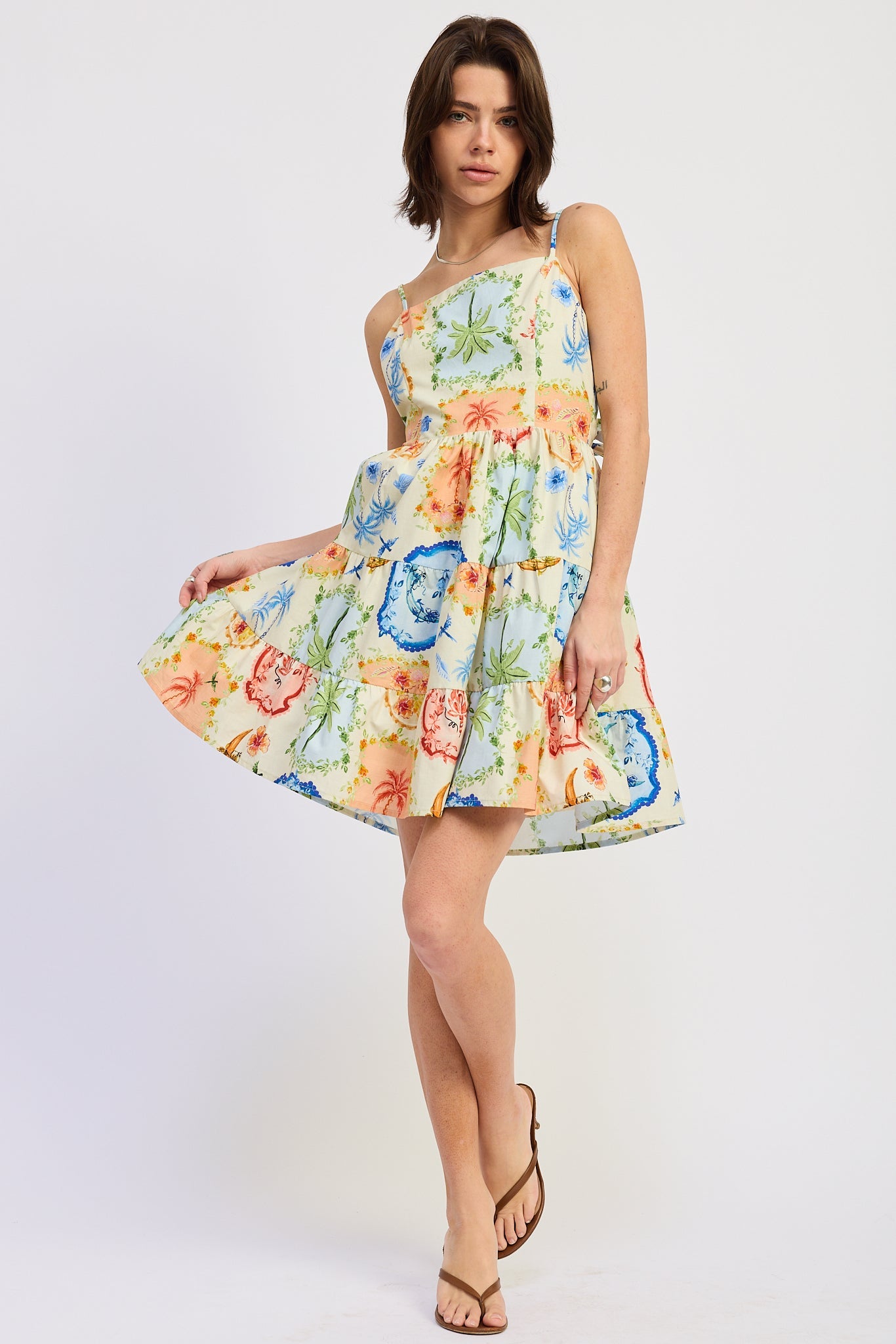 Woman wearing a scarf-inspired print blend of palm motifs and delicate detailing for a vibrant colorful floral tiered mini dress on a white background
