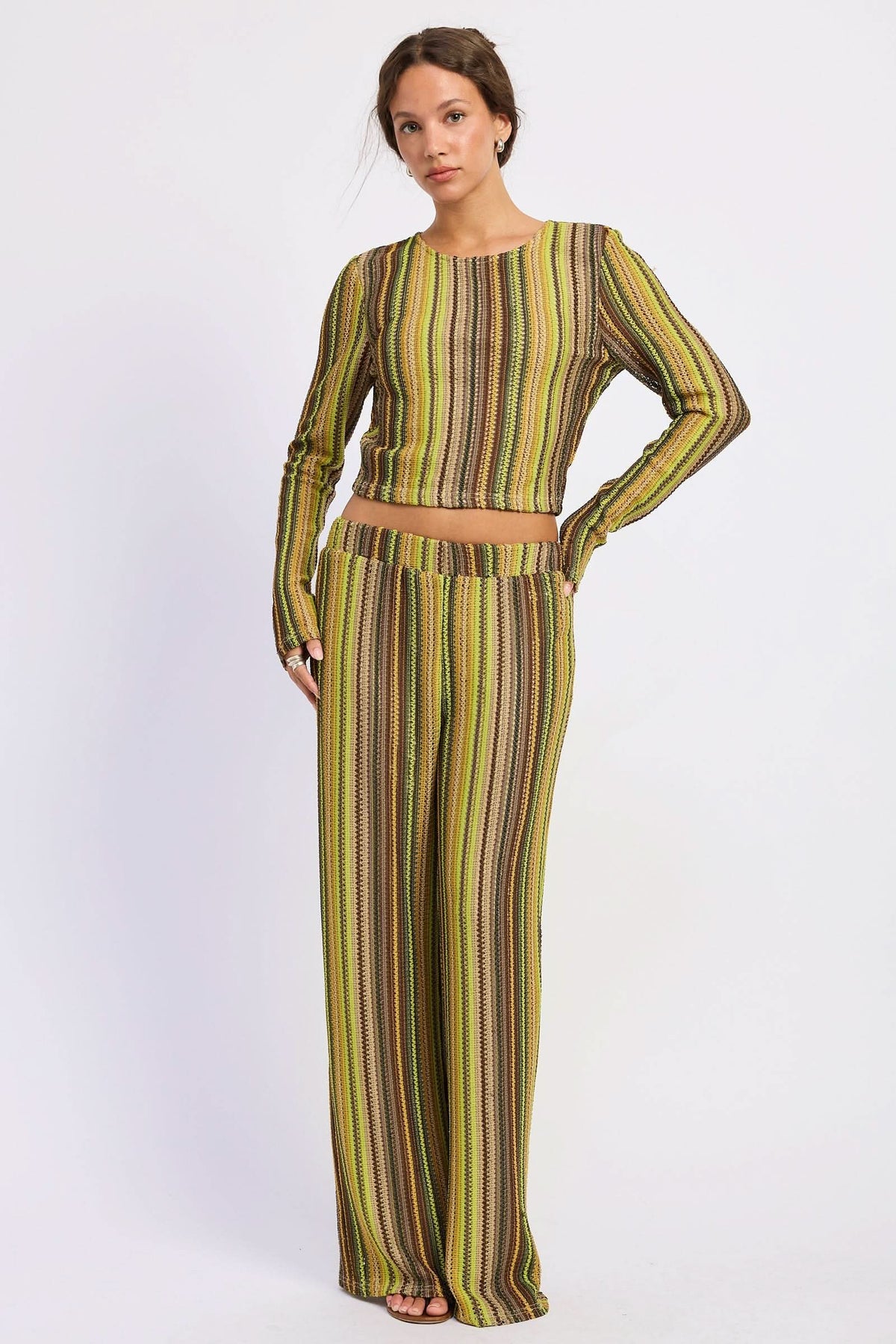 Woman wearing green and brown striped open-back top with matching wide-leg pants against white background.