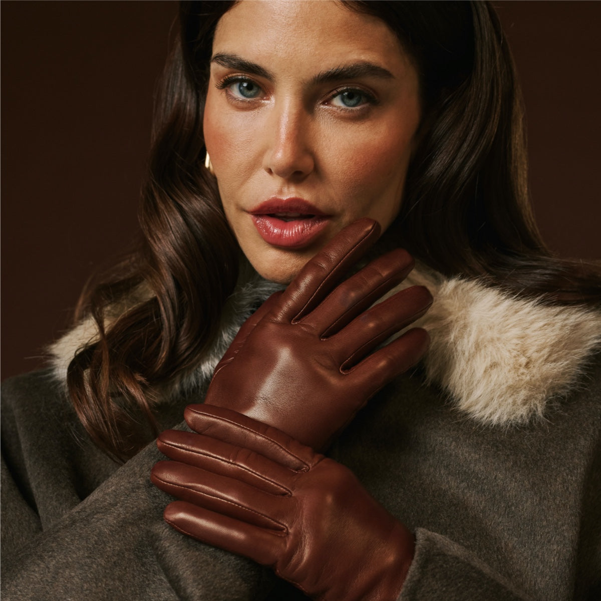 Woman wearing brown leather gloves and a fur-lined coat against a dark background