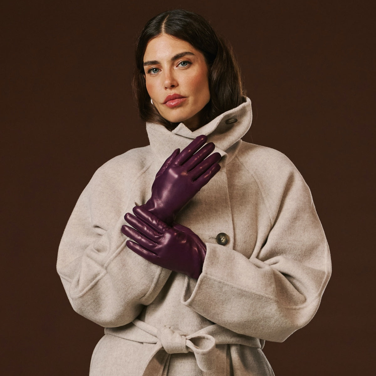 Woman wearing a beige coat and purple leather gloves against a brown background