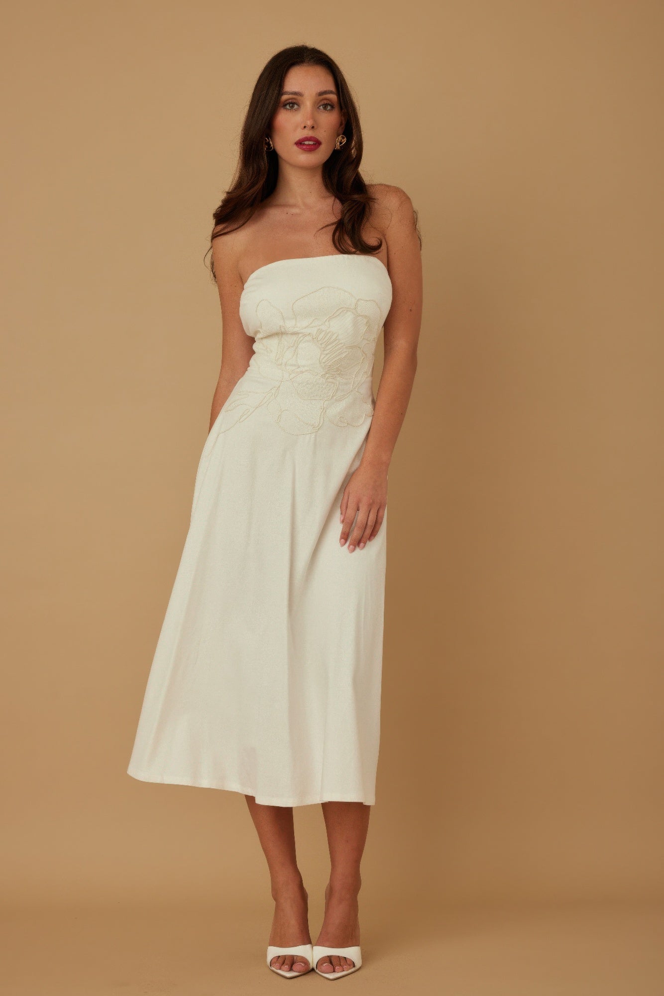 Model standing front-facing in ivory strapless midi dress with floral embroidery at bodice