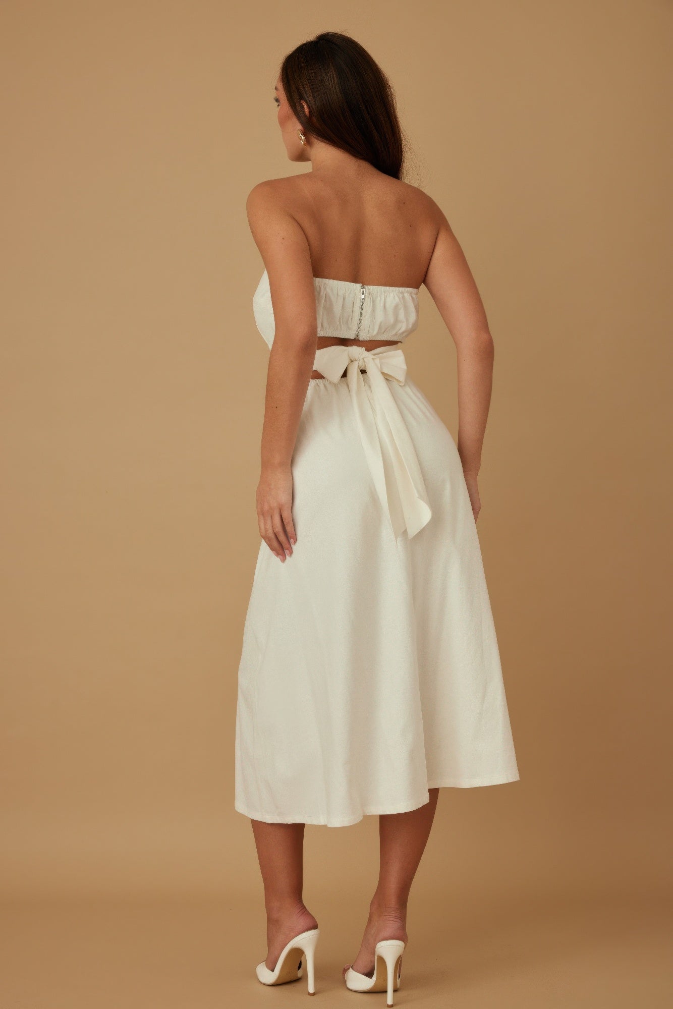 Back view of ivory strapless midi dress featuring smocked top and tie-back bow detail