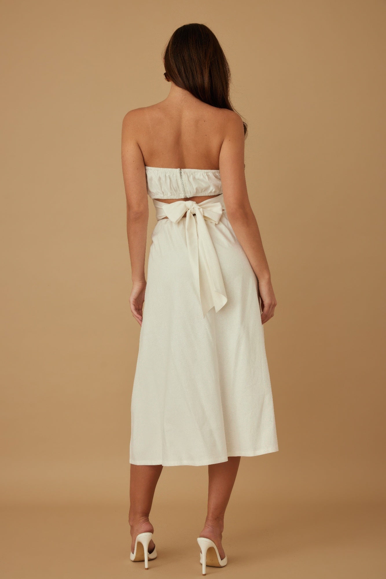 Back view of ivory strapless midi dress featuring smocked top and tie-back bow detail