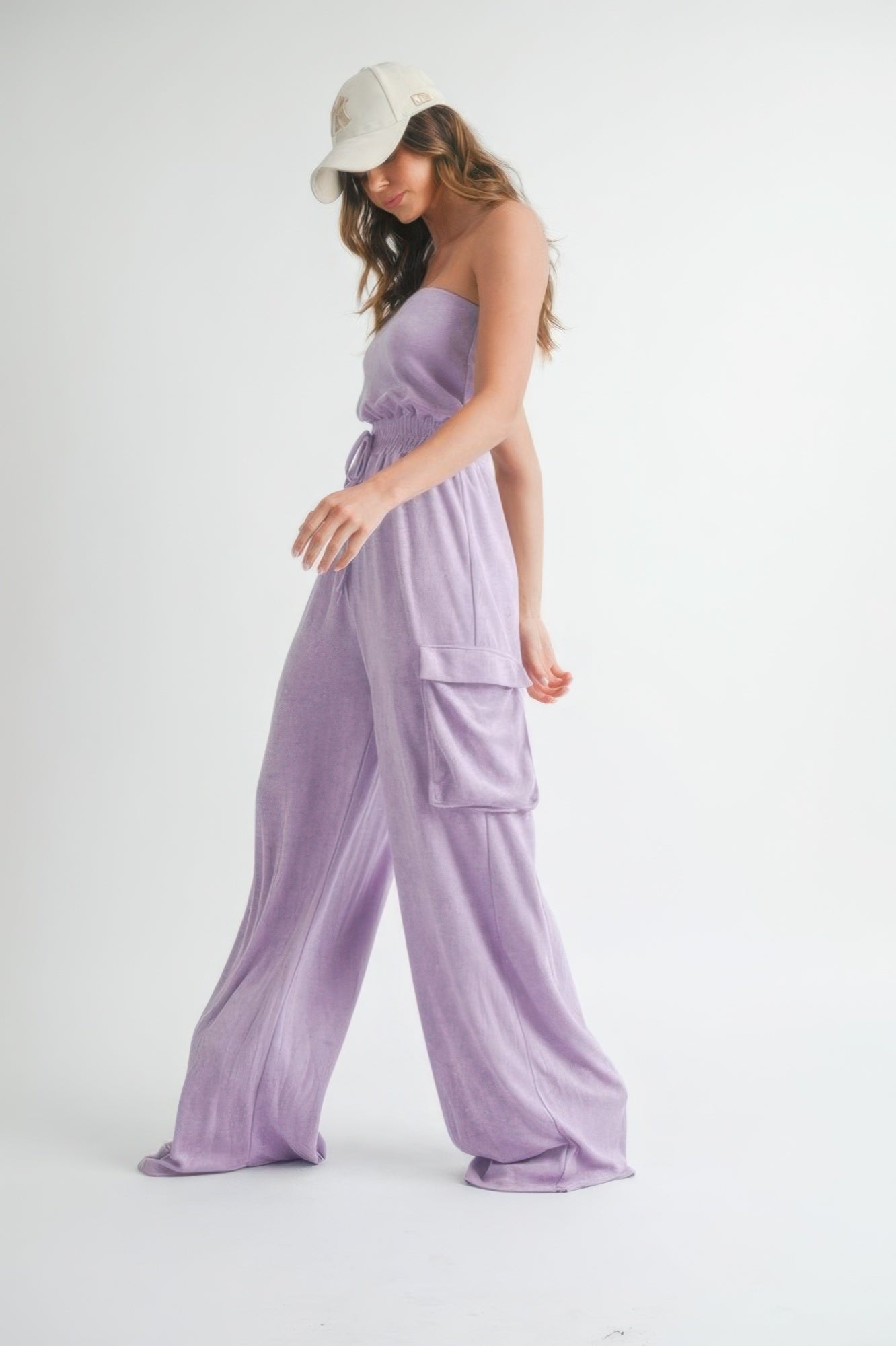 Side view of model walking in lavender strapless jumpsuit with cargo pockets