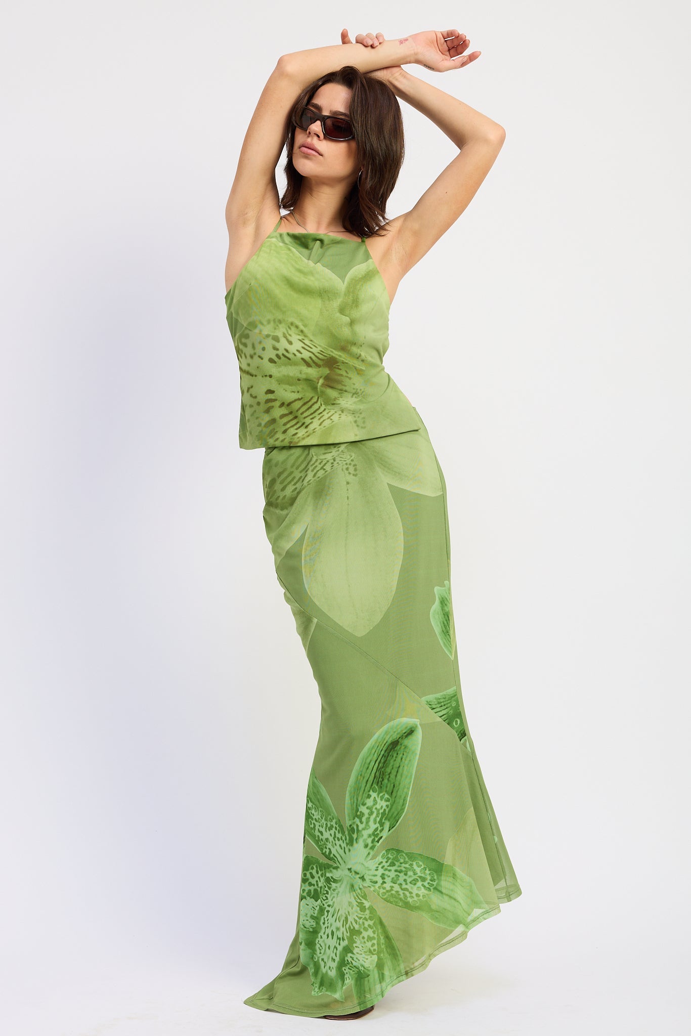 Woman wearing a green orchid print floral maxi skirt and matching open back cami top with slim straps sleeveless top with a white background front view