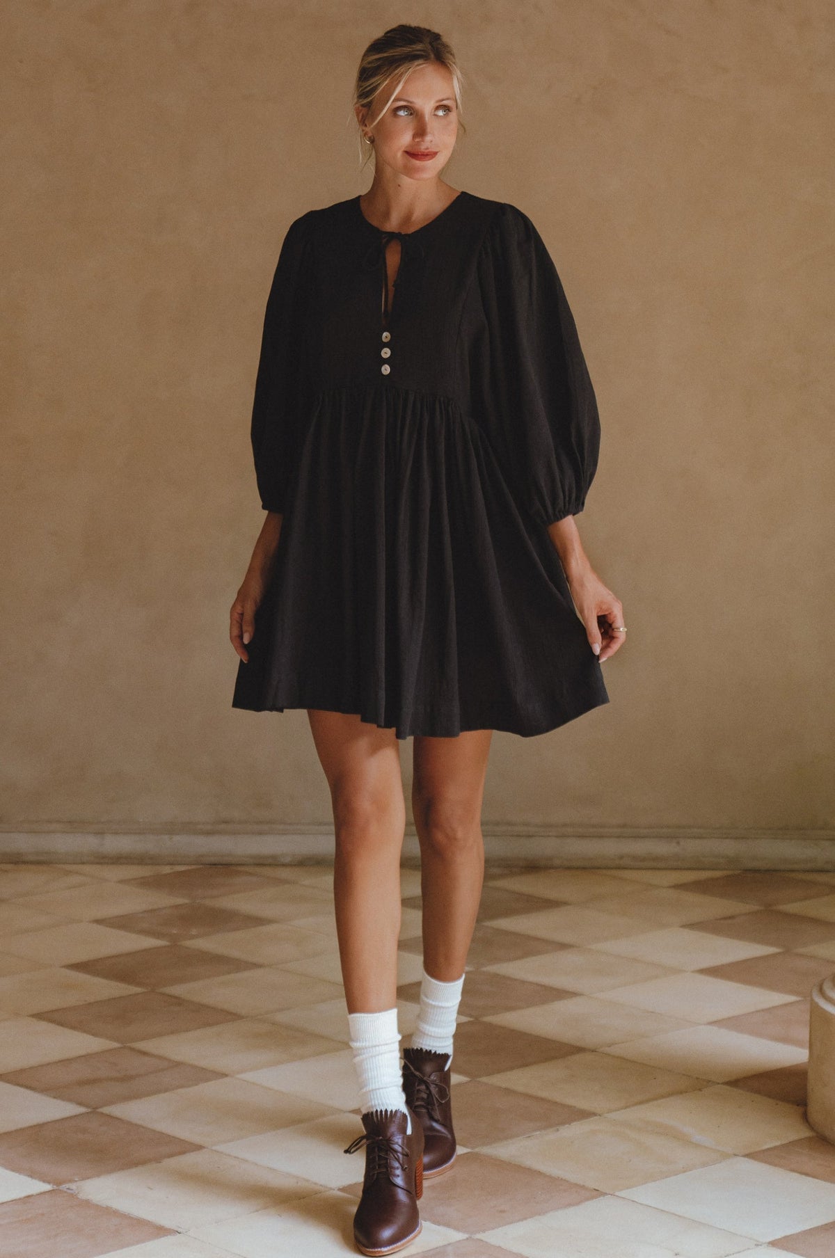 Woman wearing a black dress with long sleeves in a room with a checkered floor.
