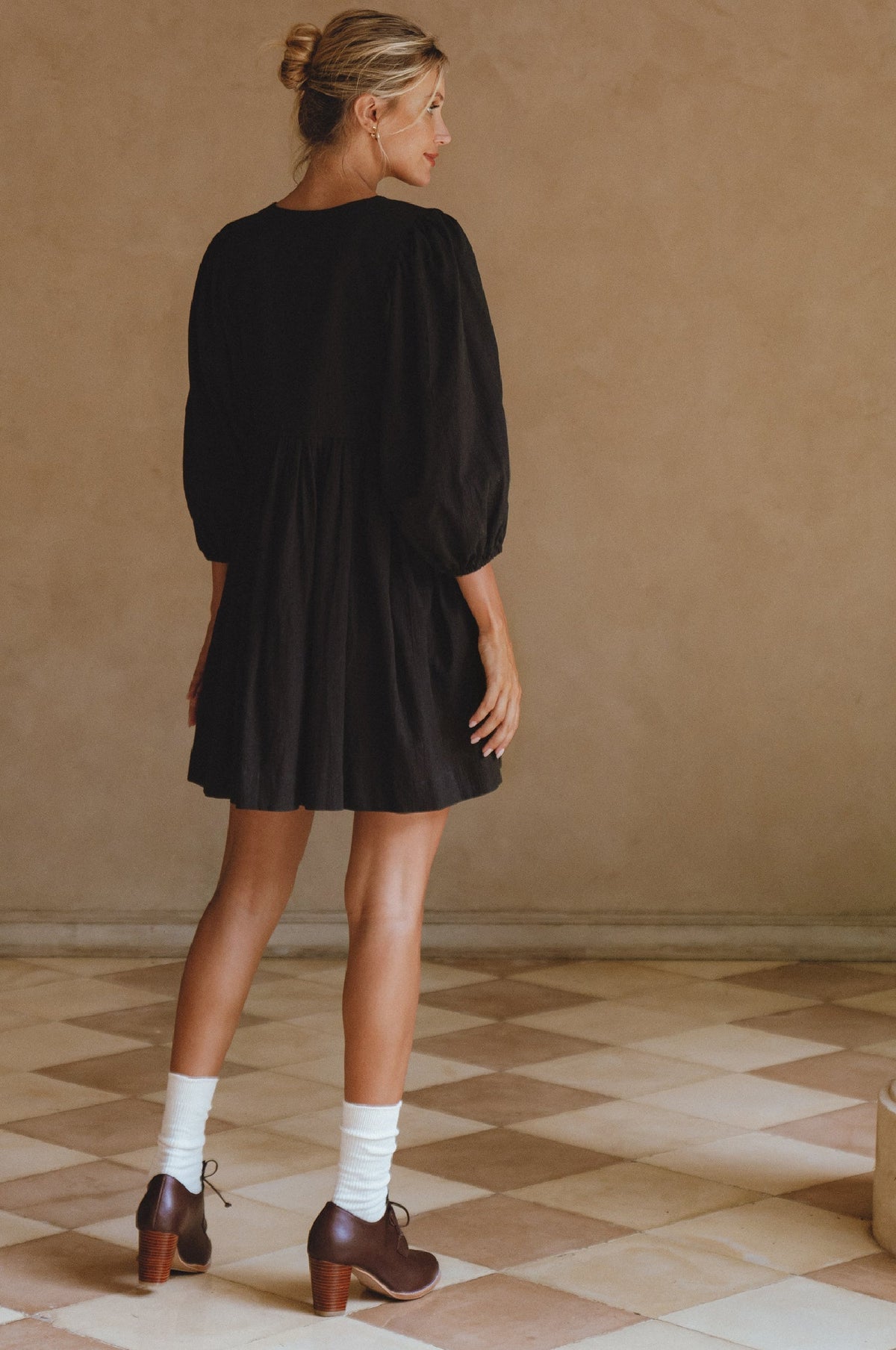 Woman wearing a black dress standing in a room with a checkered floor.