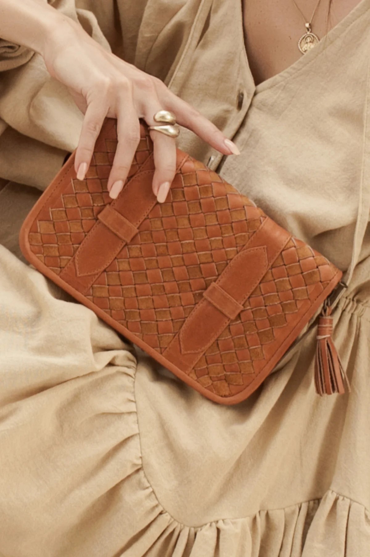 Tan woven handbag held by a person wearing a beige dress.