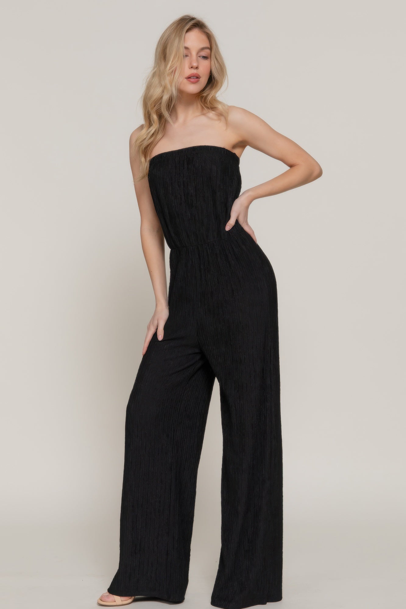 Angled pose of model in black wide-leg strapless jumpsuit