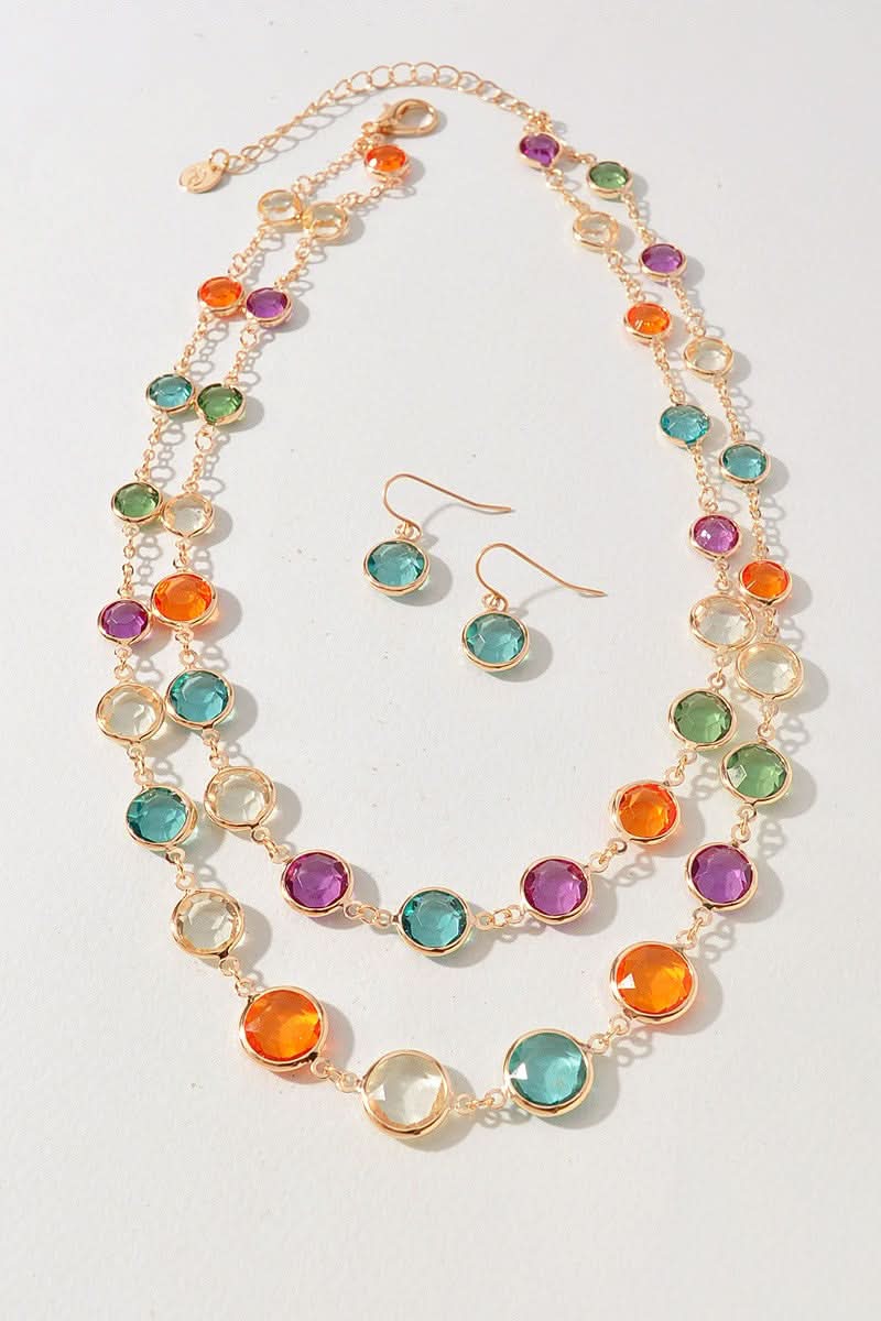 A gold-tone jewelry set featuring a multi-strand necklace and matching drop earrings, embellished with round, faceted gemstones in vibrant shades of orange, teal, green, purple, and clear, displayed on a light off-white background.