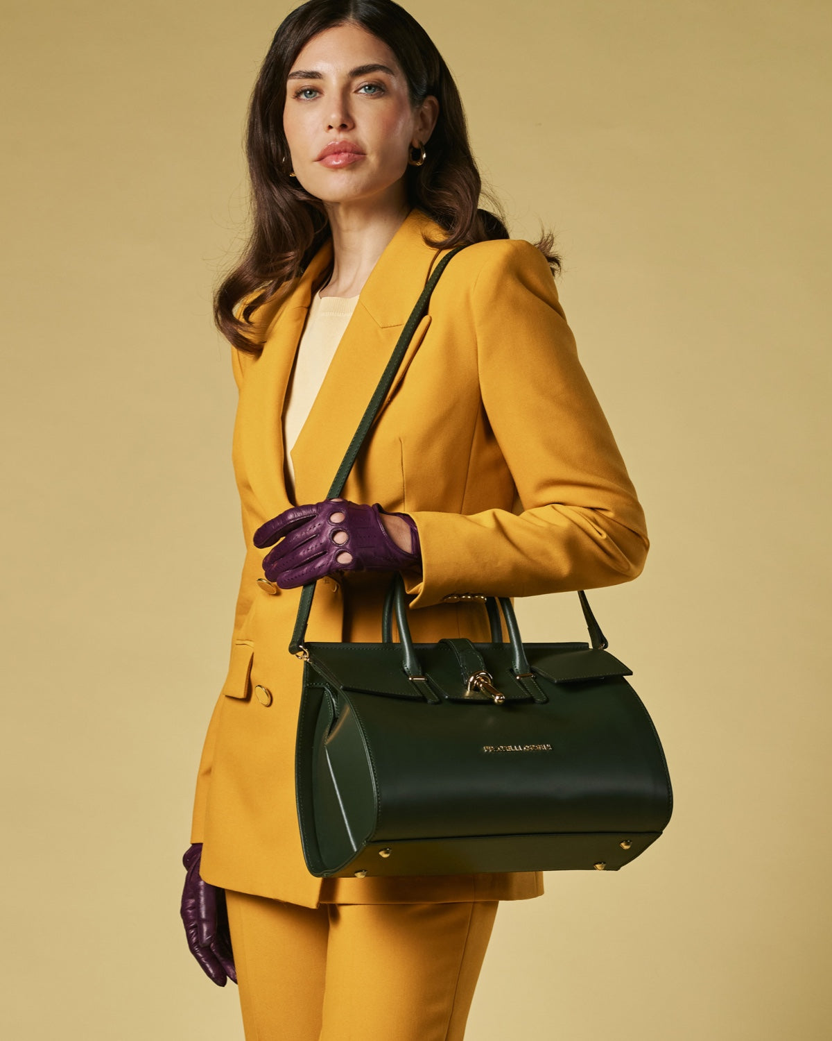 Woman in a yellow suit holding a black handbag against a beige background
