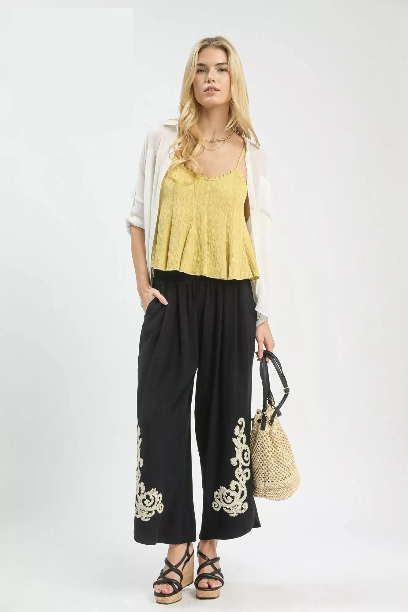 Model wearing black linen blend wide leg pants with ivory embroidered hem, elastic waistband, side pockets, and wedge sandals.