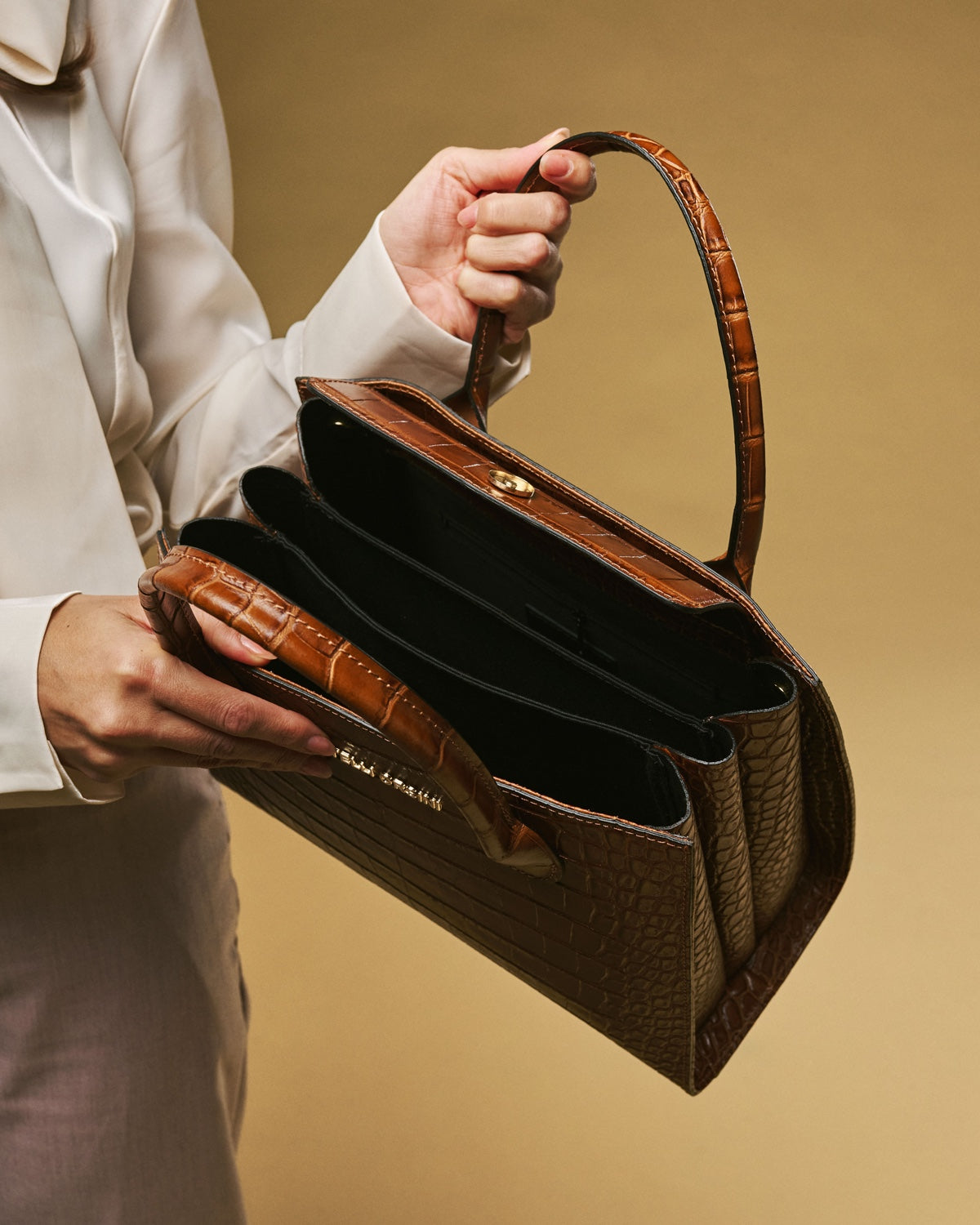 Brown handbag held by a person against a beige background