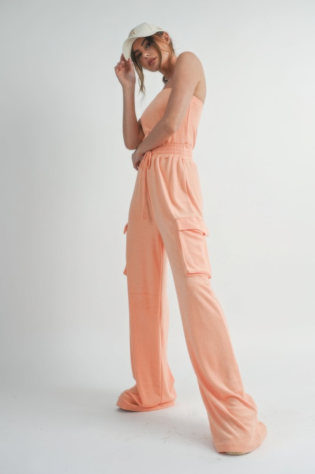 Model wearing peach strapless jumpsuit with smocked waist and cargo pockets.